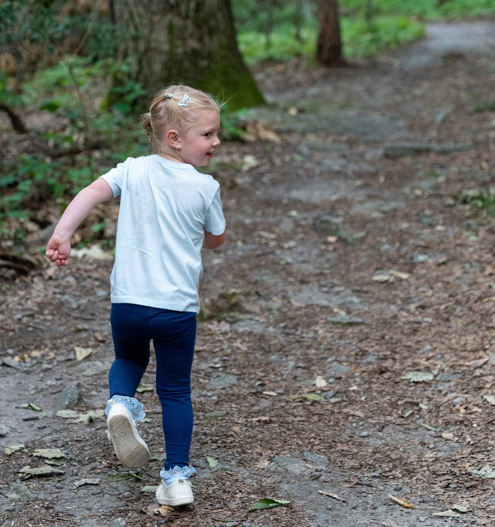 A toddler running ahead of her parents on a rocky woodland trail