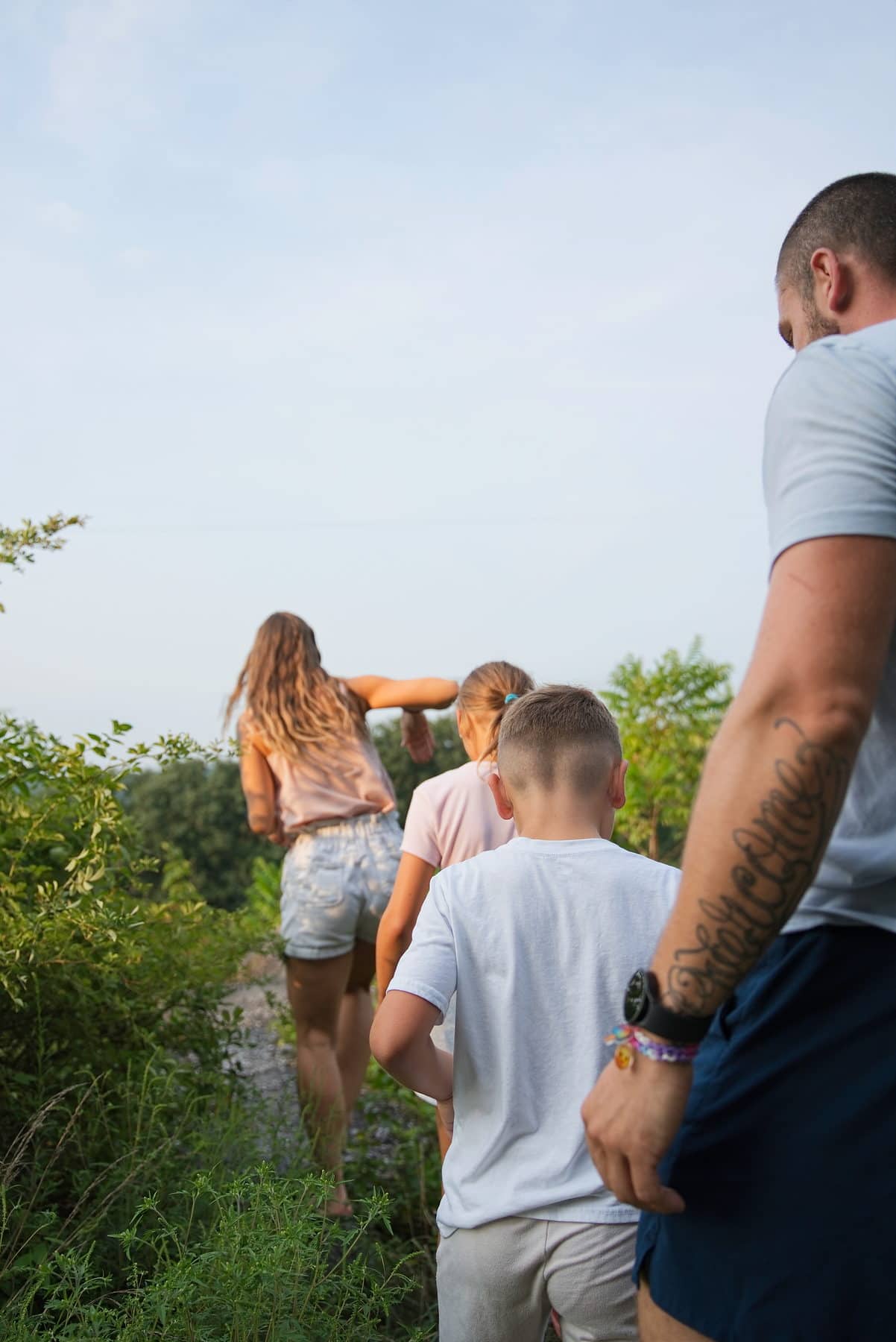A family climbing a wooded hillside in backlit summer evening light