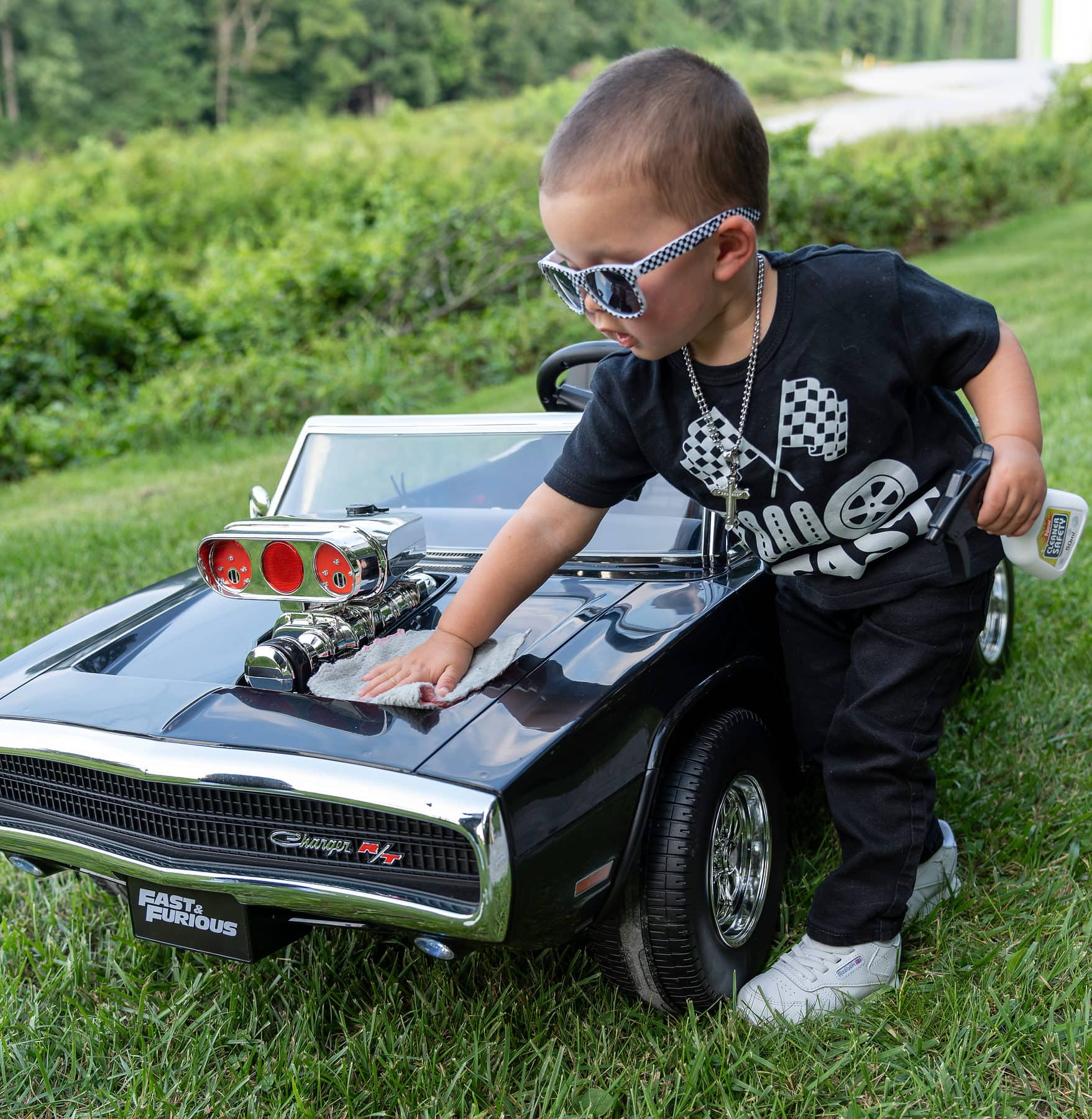 A two year old in sunglasses inspecting a toy muscle car at his birthday session