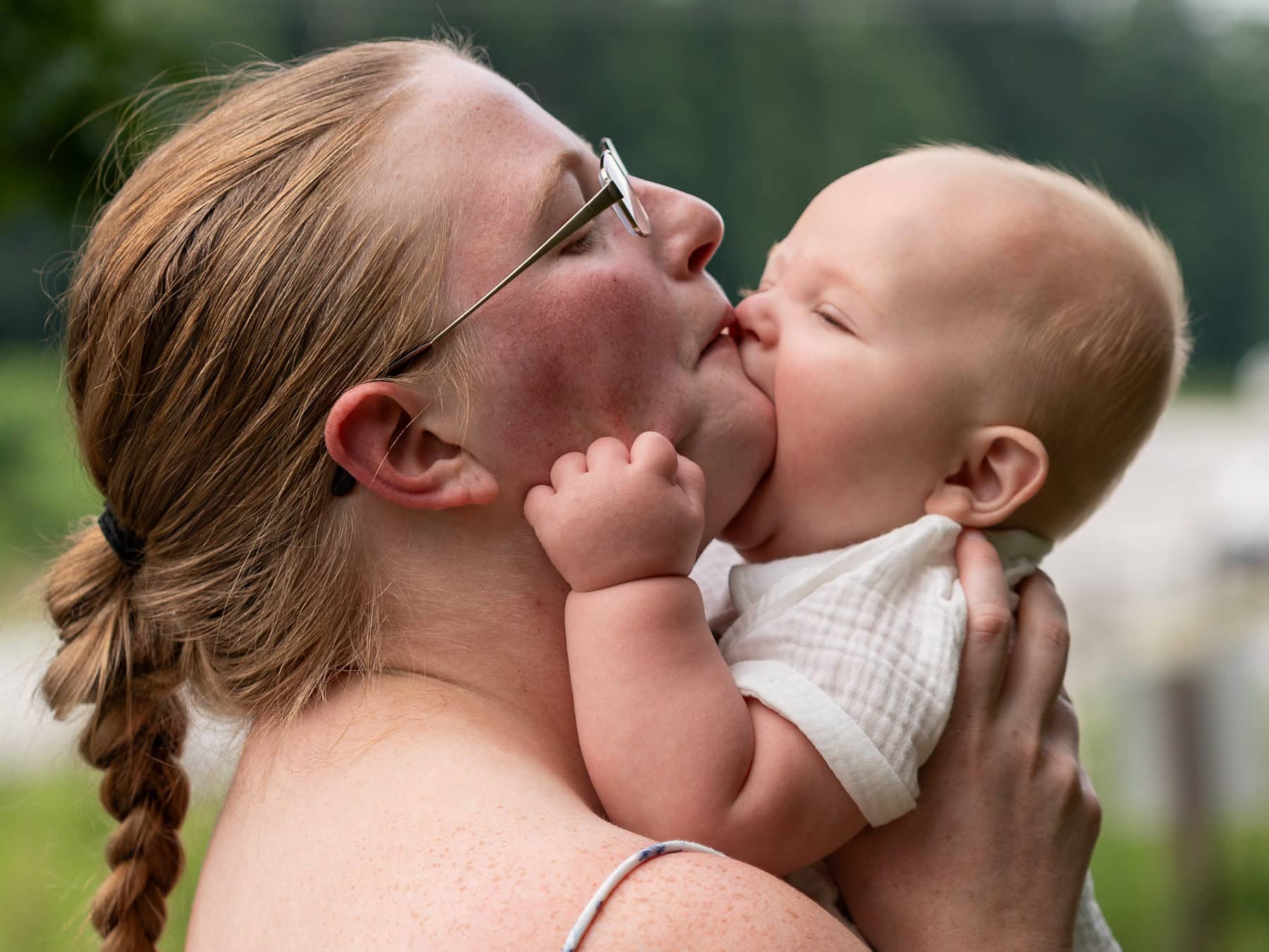 A mother kissing her baby son on the cheek in evening light