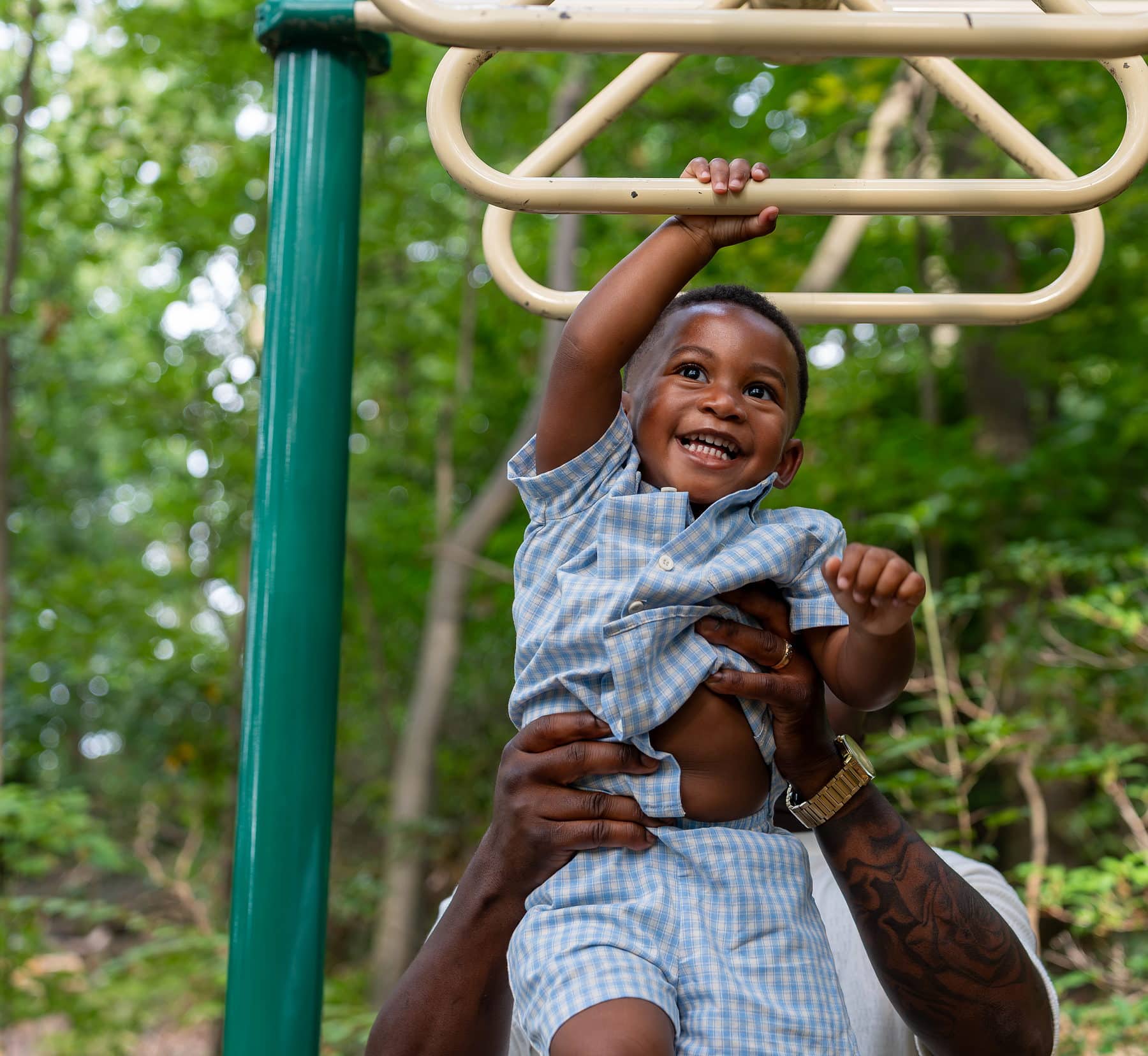 A father lifting his son up to the playground bars at eye level
