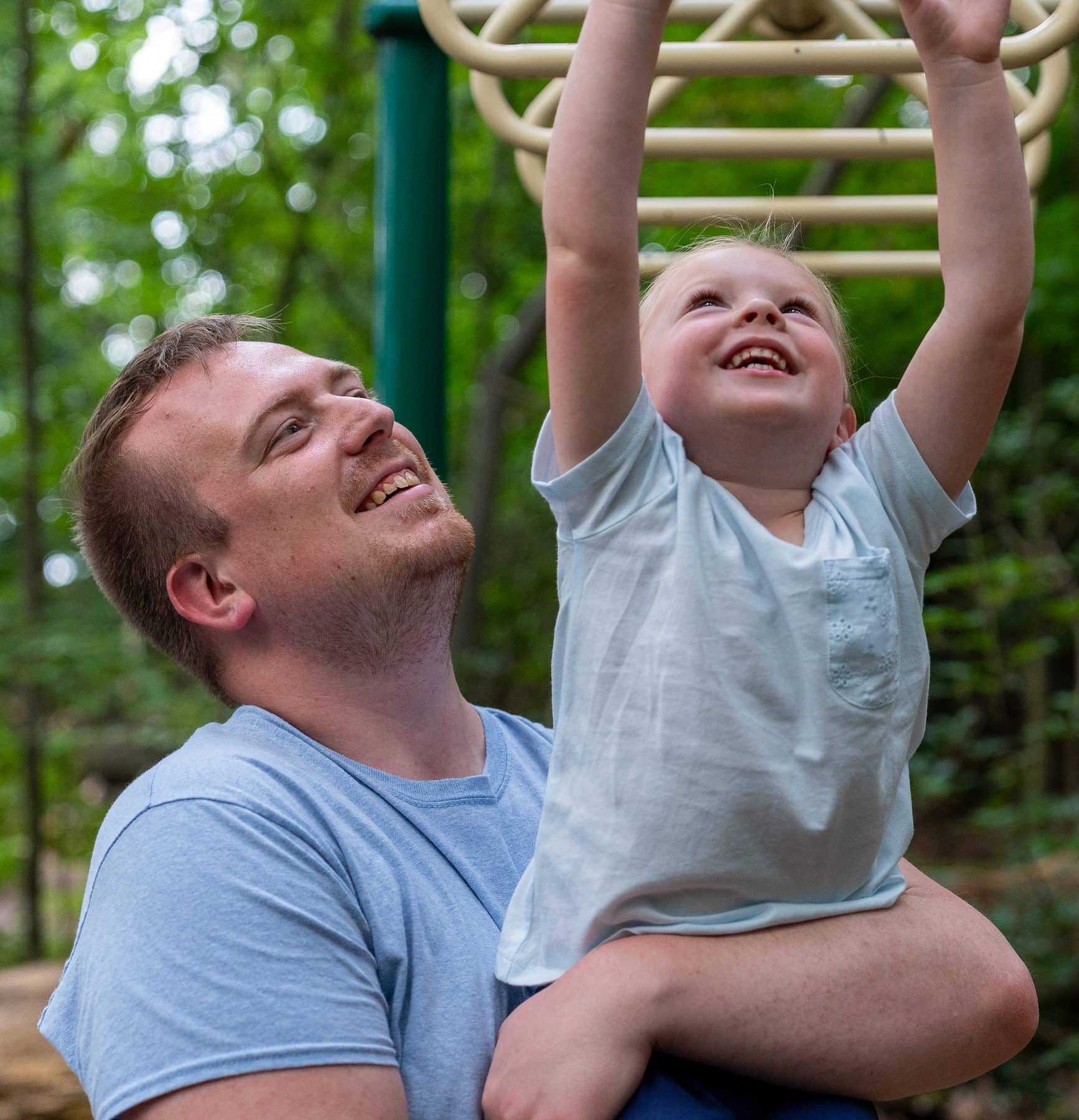 A father lifting his son to the monkey bars, both of them laughing