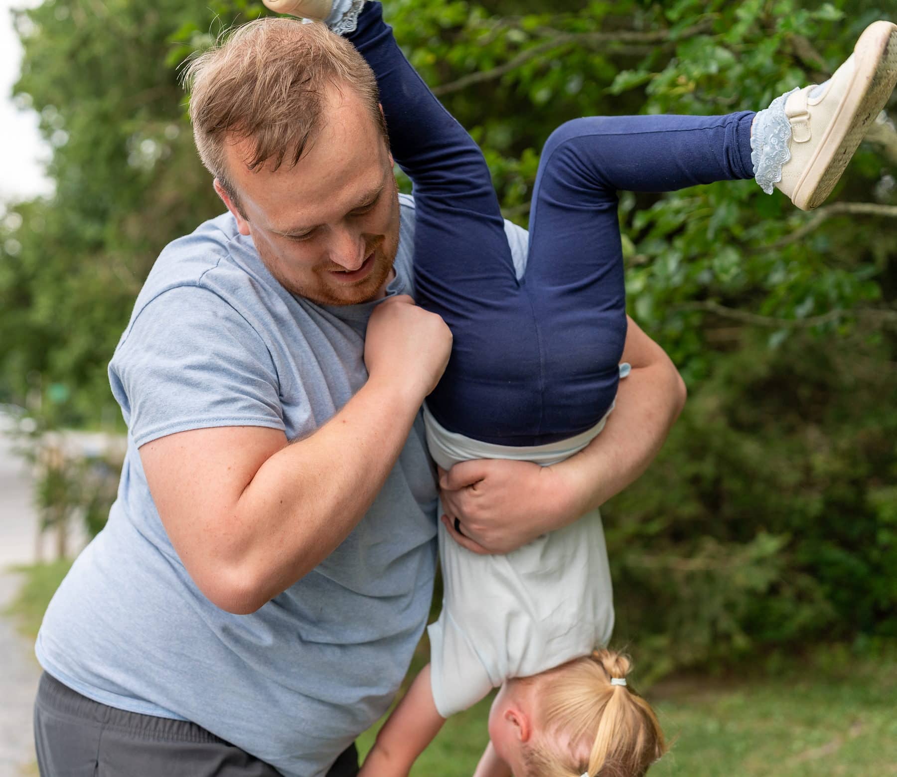 A father holding his laughing daughter upside down in a back yard