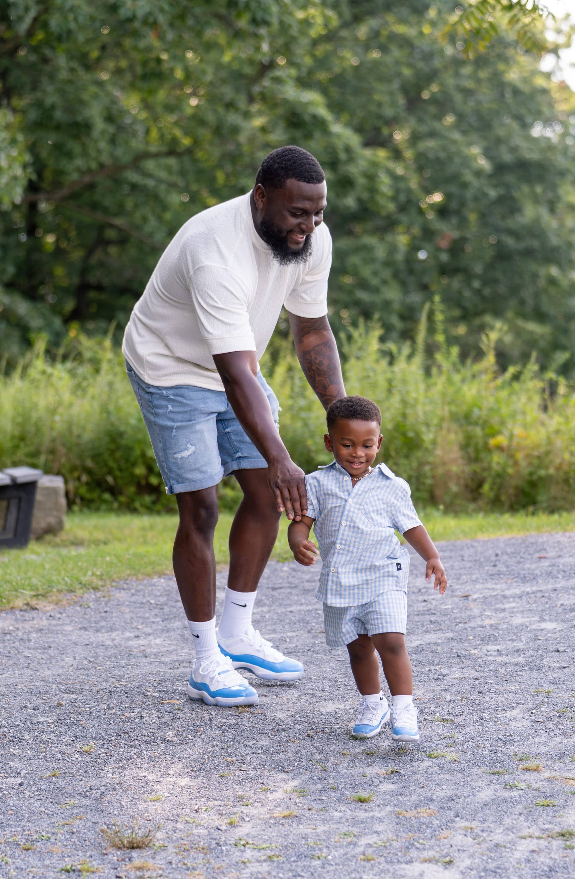 A father walking a wooded path with his young son, holding his hand