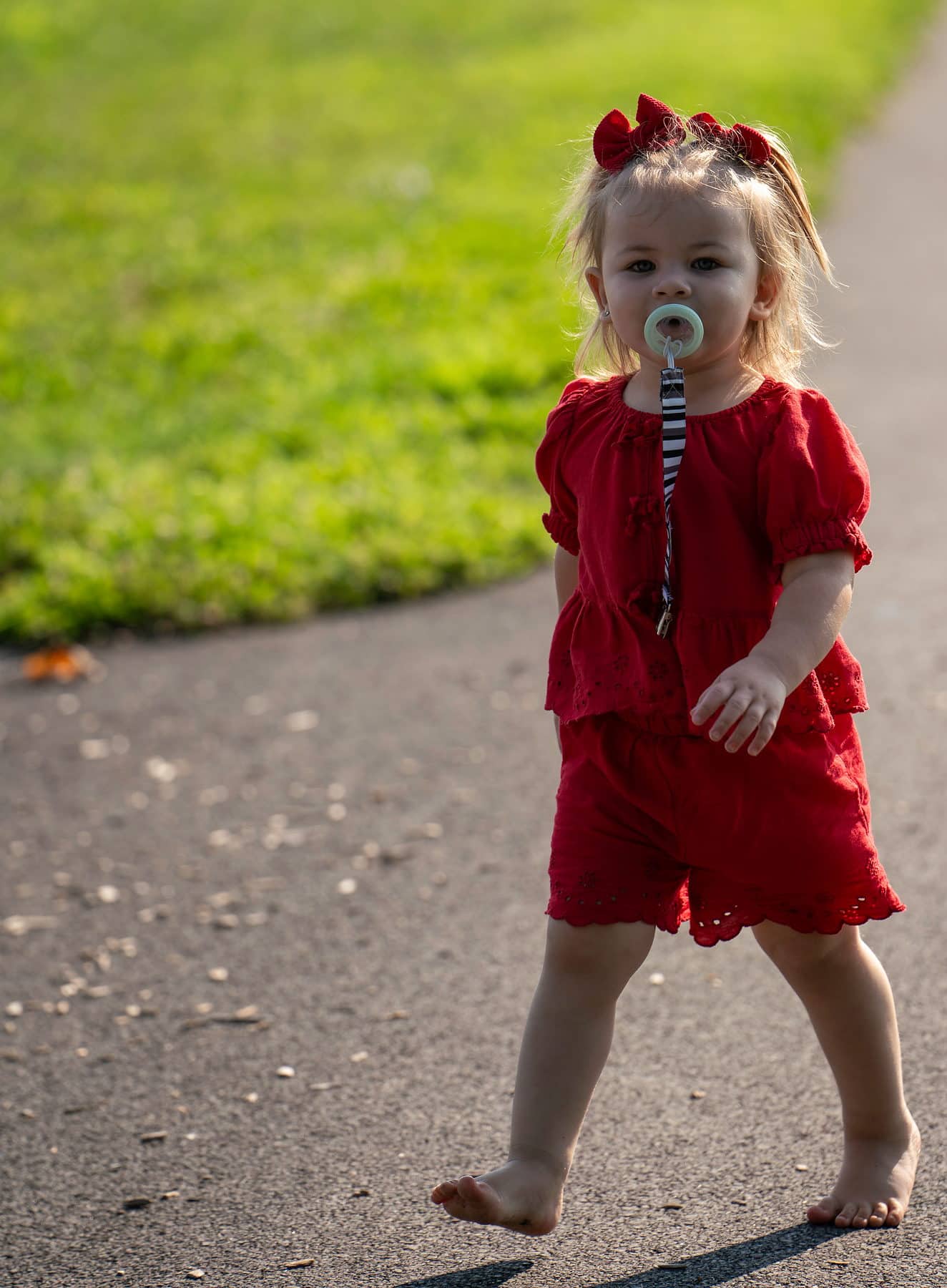A toddler walking down a park path with a pacifier and total determination