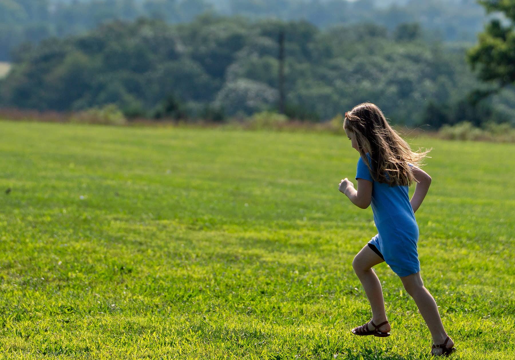 A girl running across an open green field at golden hour