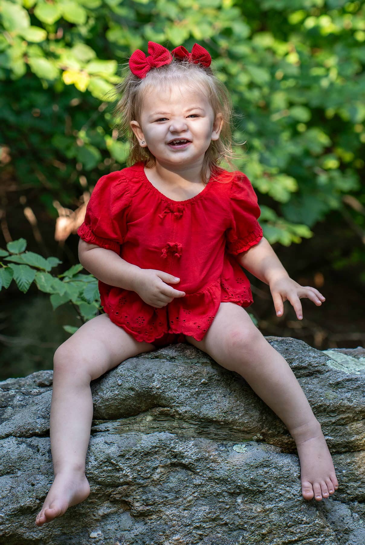 A toddler in a red romper standing on a boulder in the evening sun