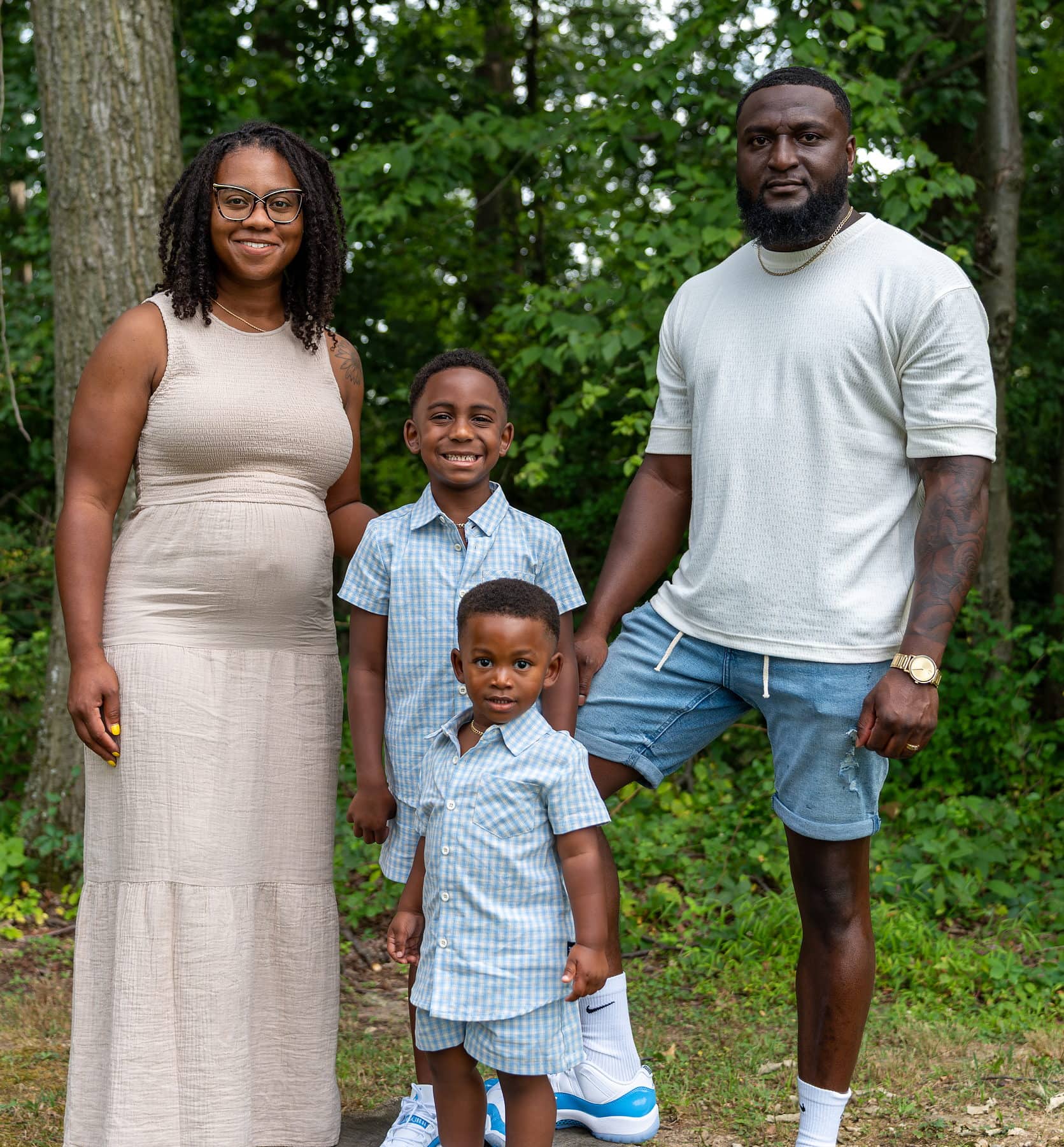 A family of four standing shoulder to shoulder at the edge of a treeline