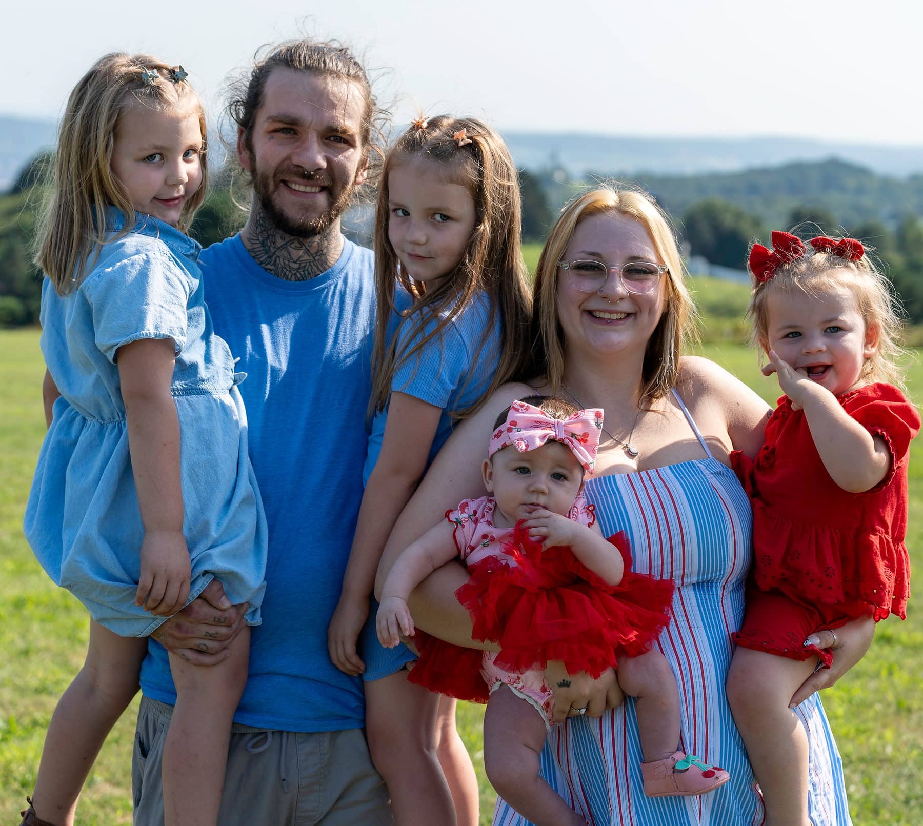 A family of six on an open hillside, four daughters gathered around their parents