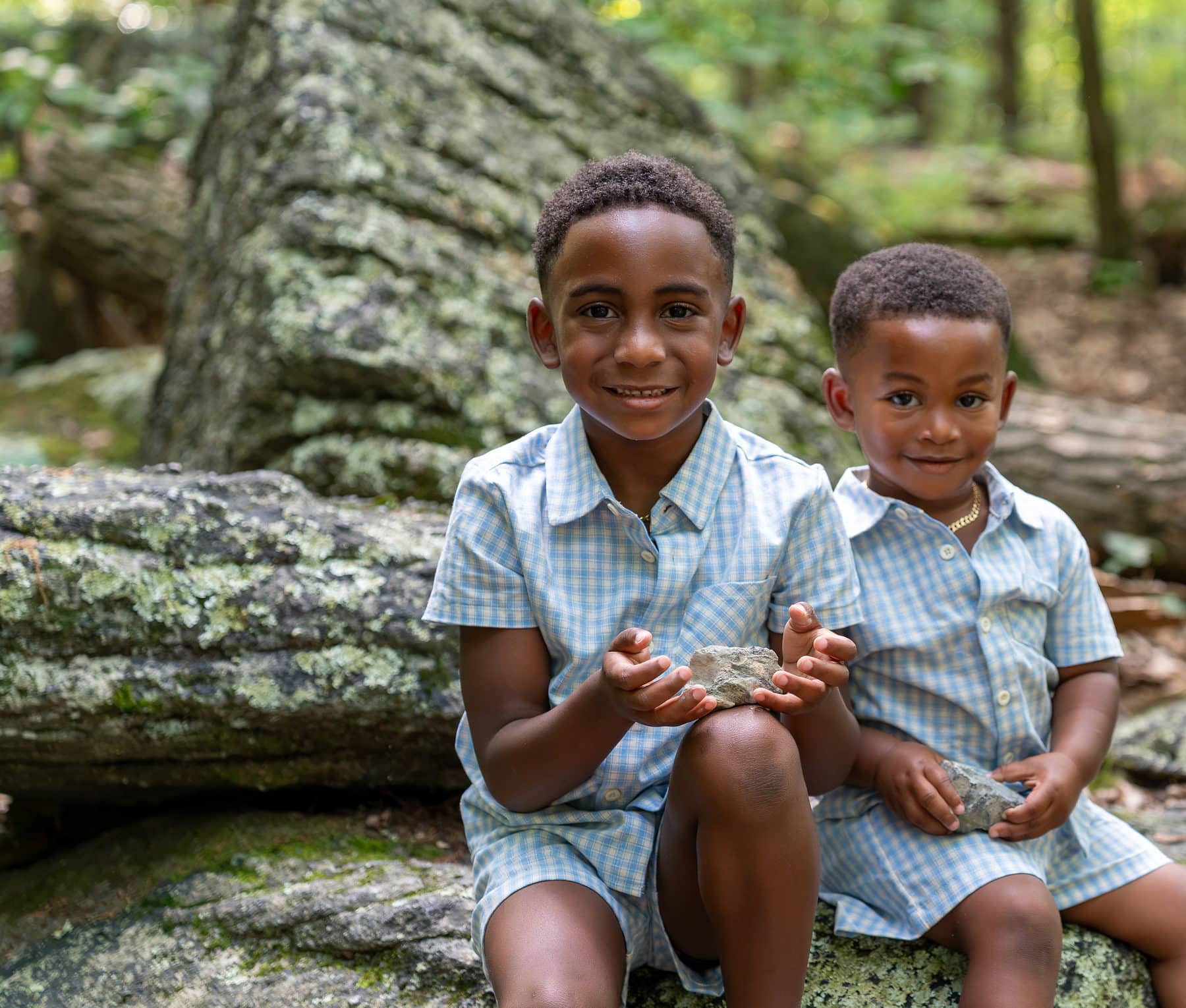 Two brothers sitting together on a large rock in the woods
