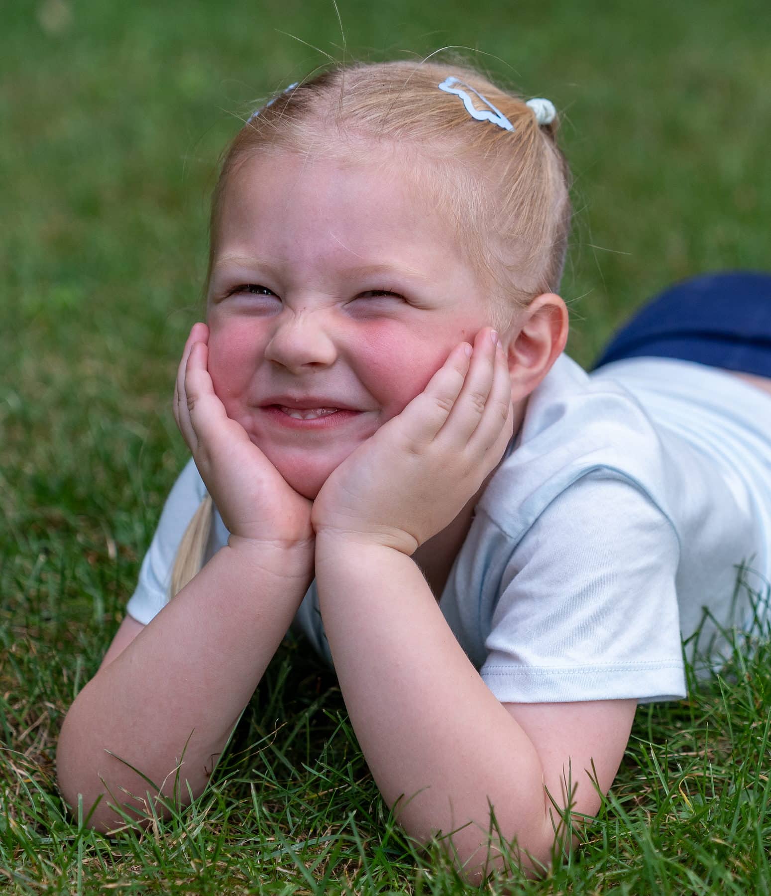 A young girl lying in the grass with her chin propped in both hands