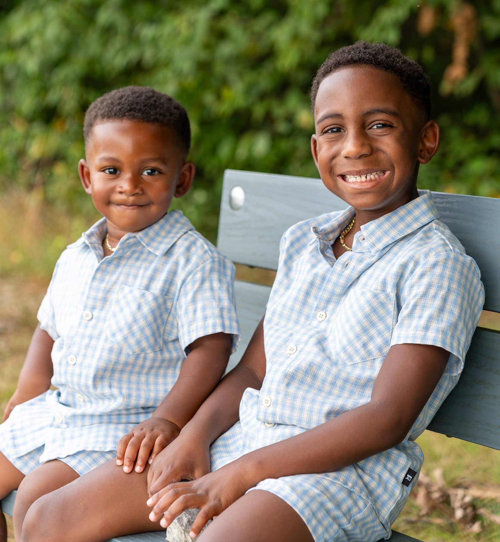 Two brothers sitting side by side on a park bench, grinning