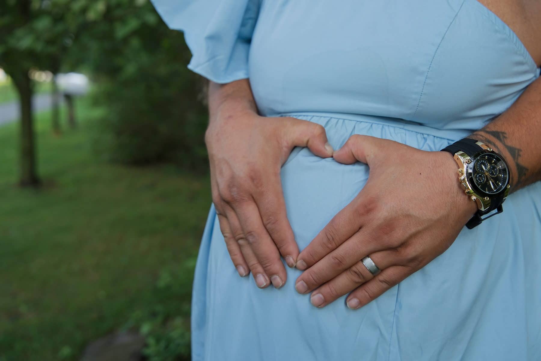 Two pairs of hands forming a heart on an expectant mother's belly