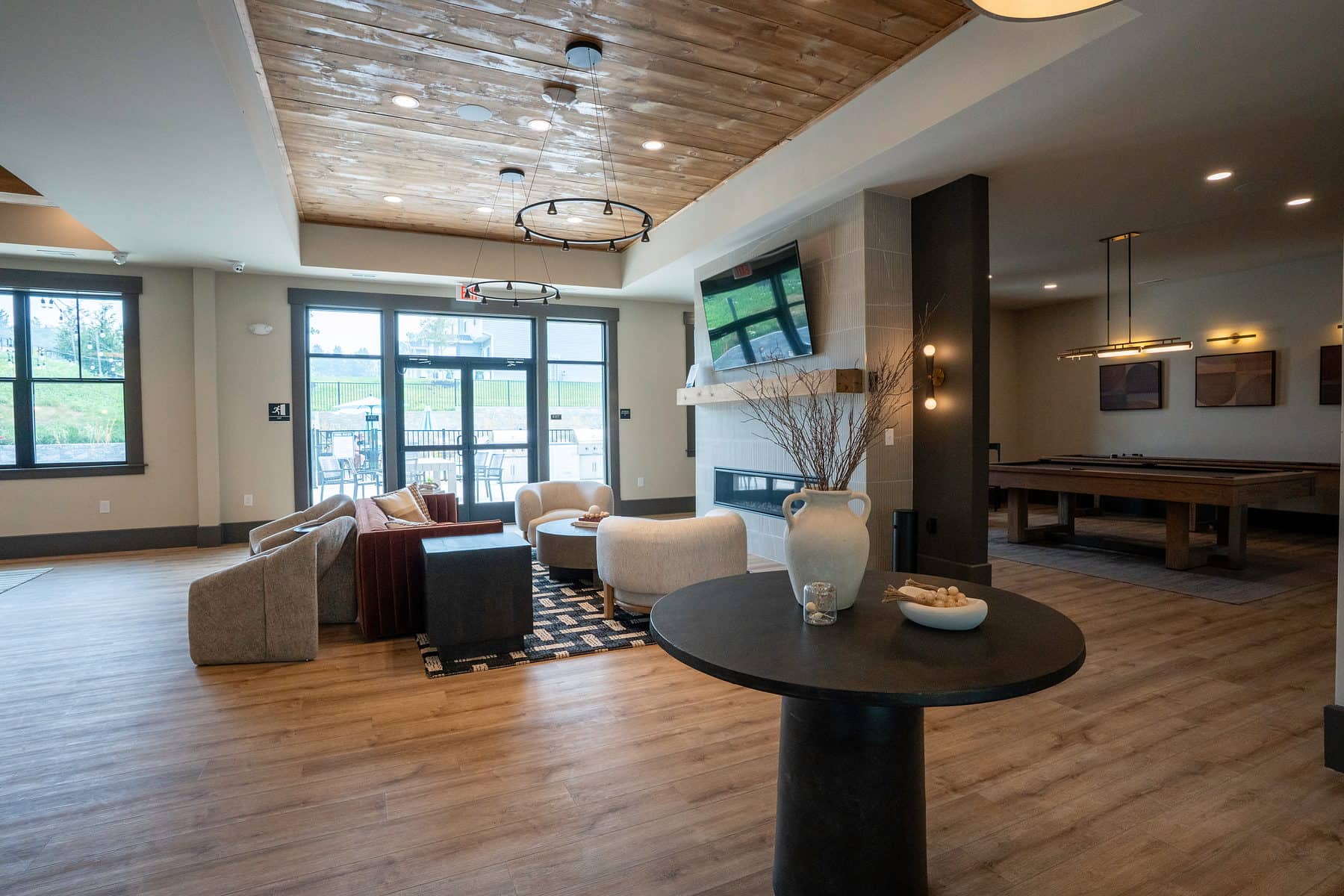 A multifamily clubhouse great room with a fireplace, wood plank ceiling and the game room beyond