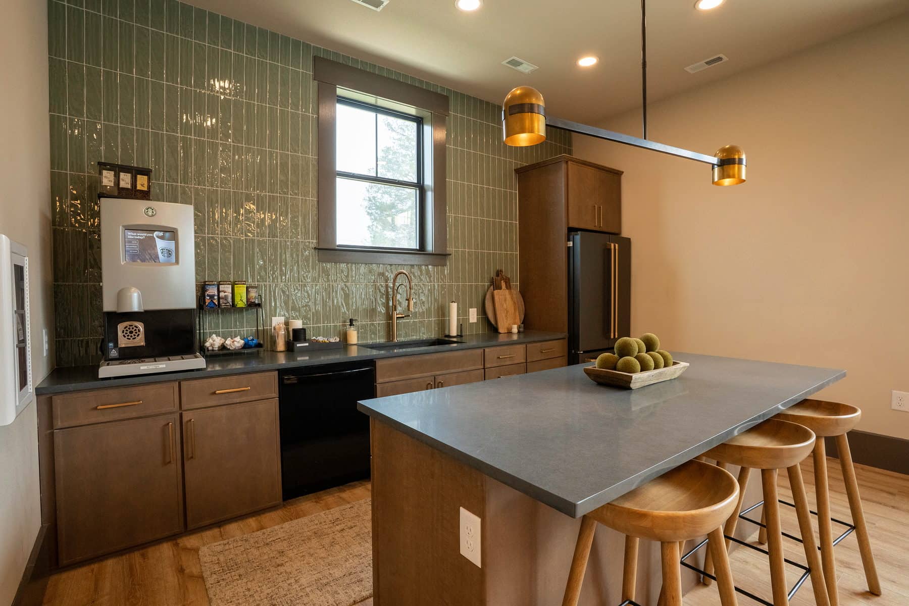 A community kitchen with a concrete island, bar stools and green tile backsplash