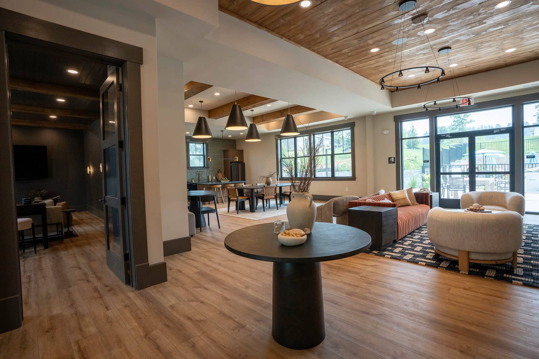 A clubhouse lounge with café tables, a patterned rug and a wood plank ceiling