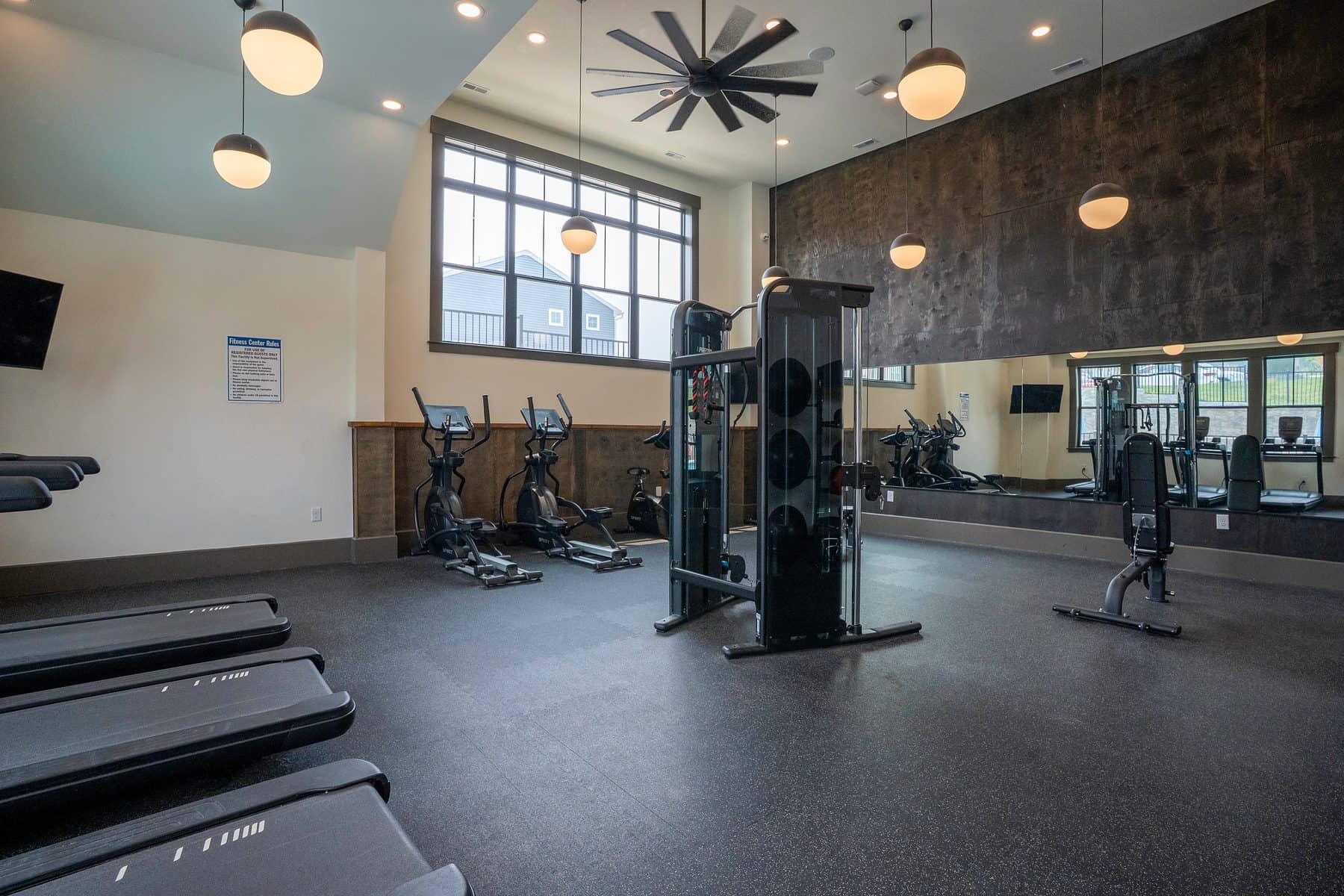 A resident fitness centre with a row of treadmills and a cable machine under tall windows