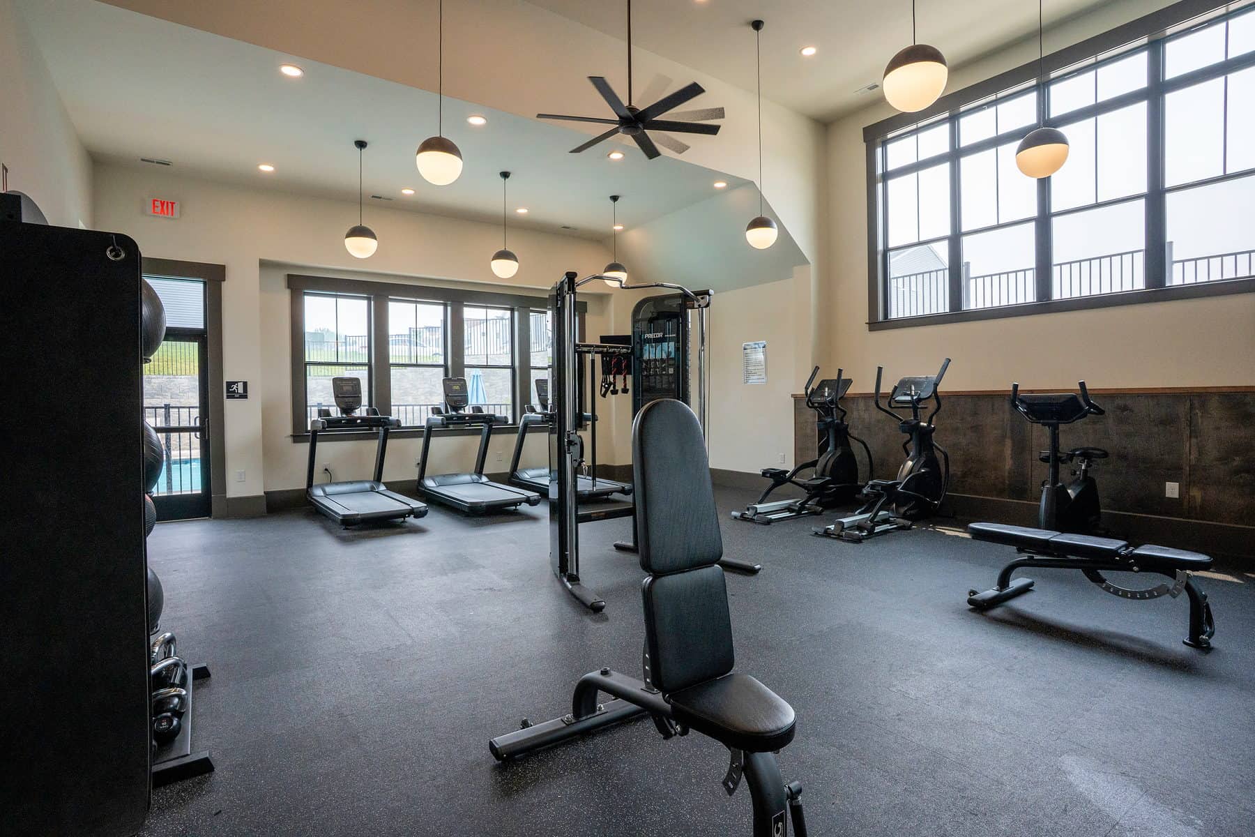 A resident fitness centre photographed wide, showing equipment, ceiling fans and windows