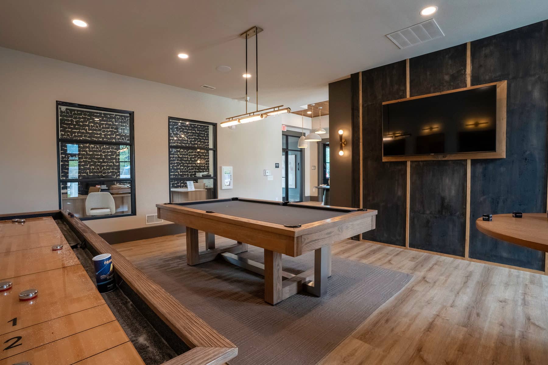 A community game room with a shuffleboard table and a dark feature wall