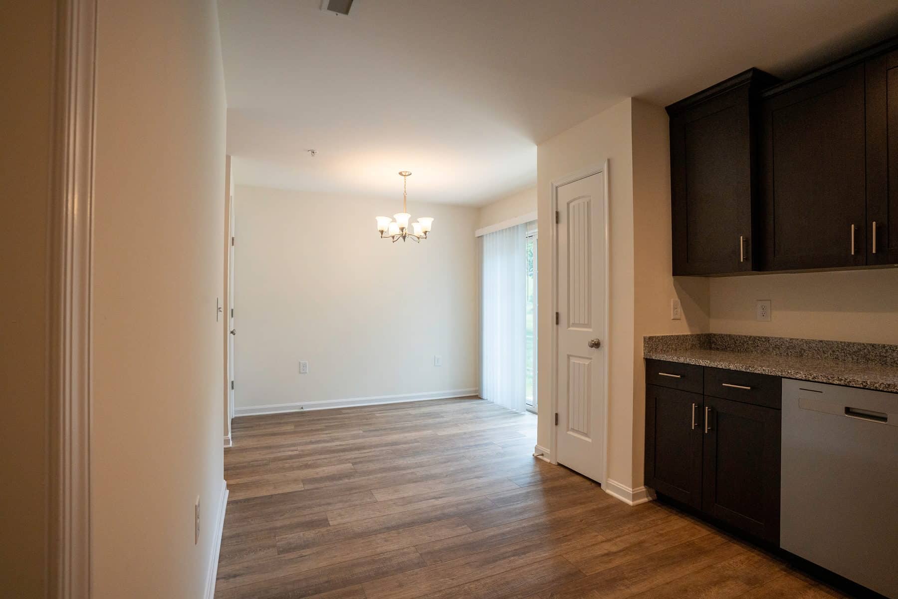 An empty apartment kitchen opening to a dining area under a chandelier