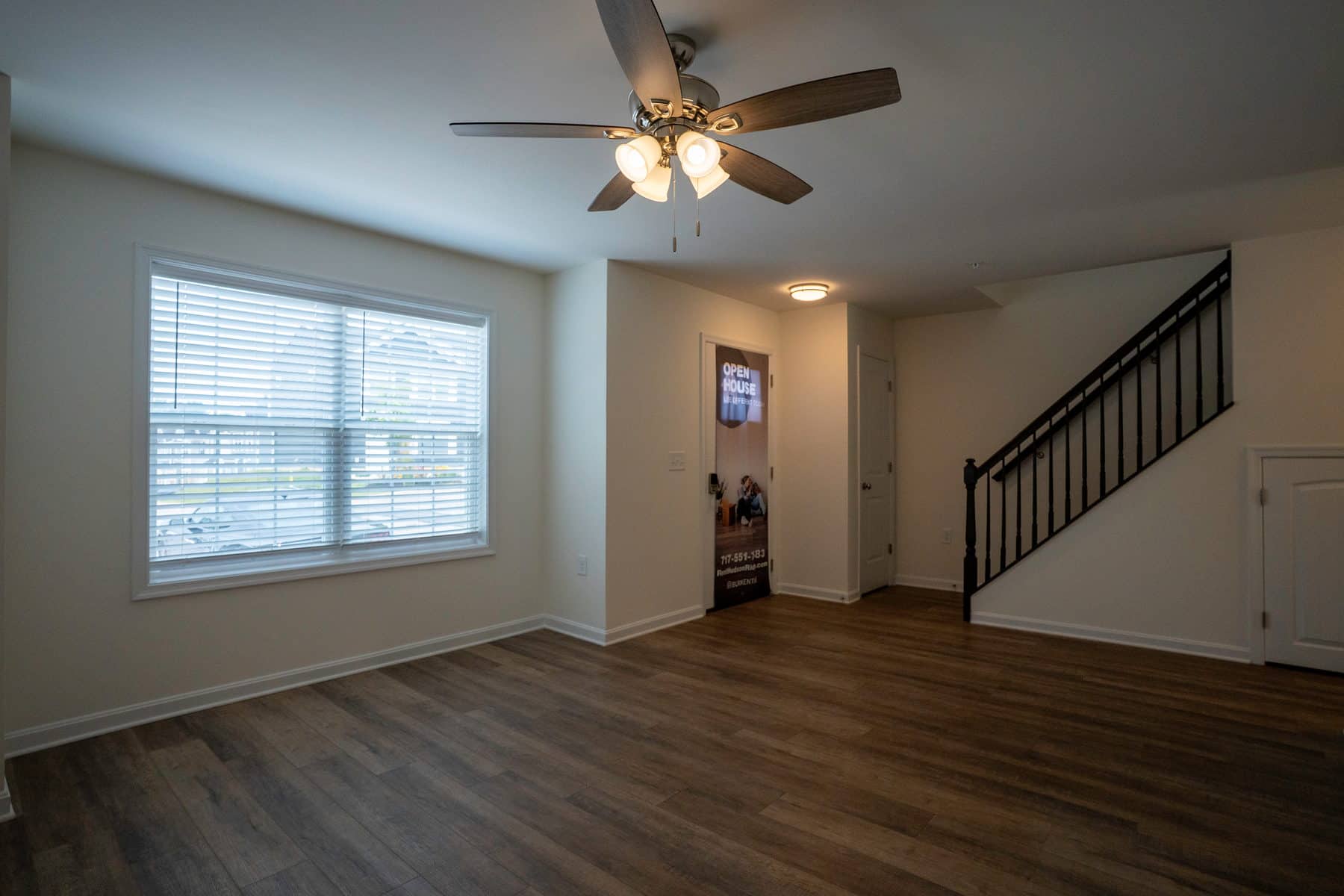 An empty apartment living room with plank flooring, a stair rail and window light
