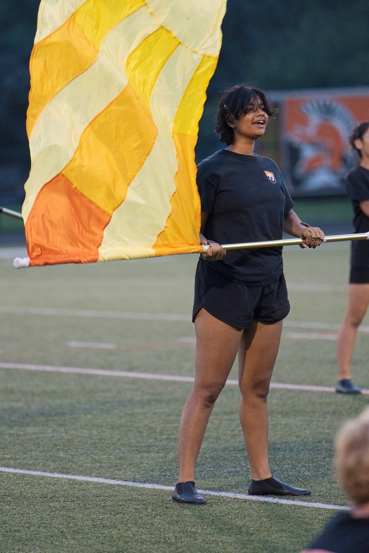 A marching band color guard member raising a flag against a dusk sky