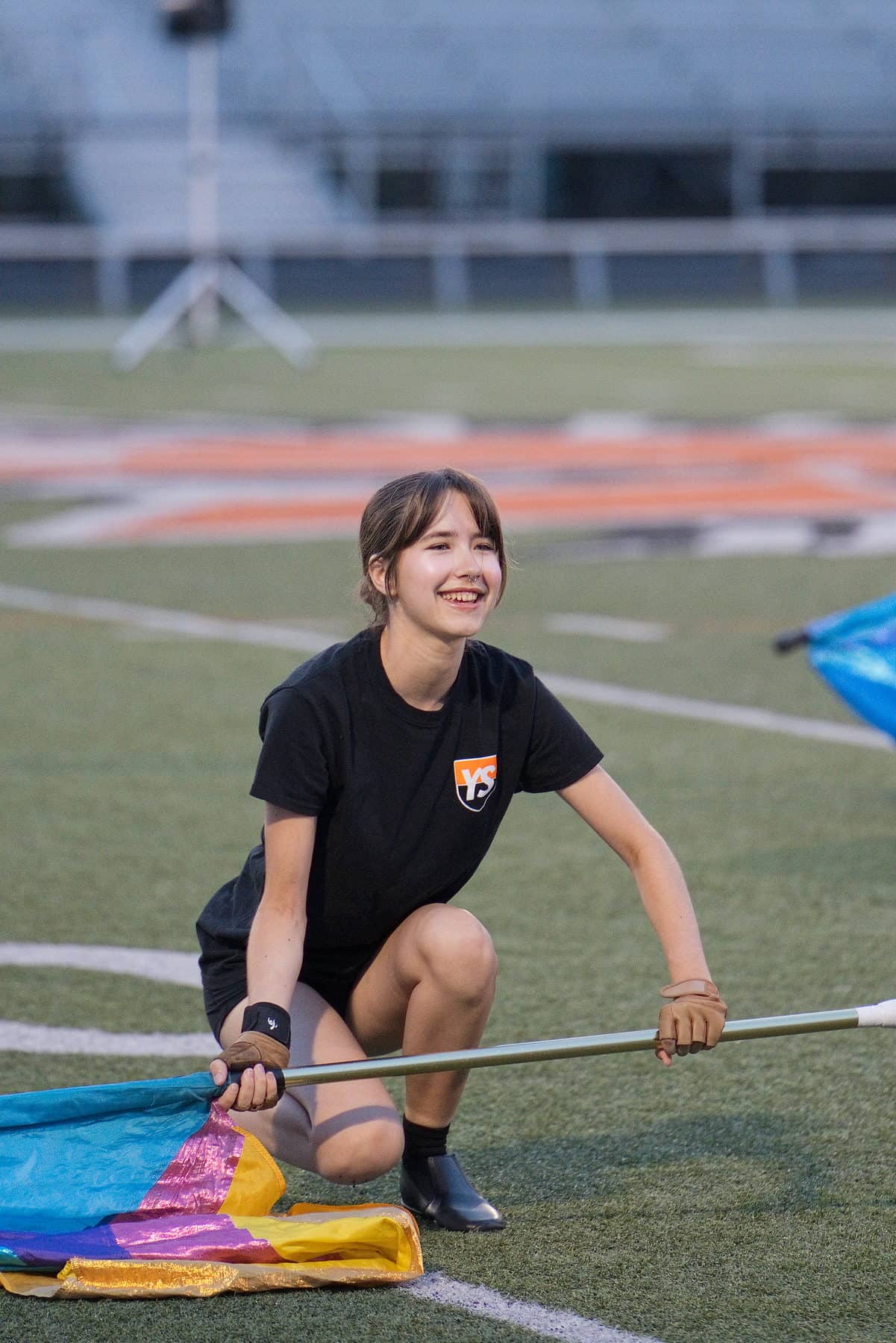 A color guard member kneeling with her flag during a break in rehearsal