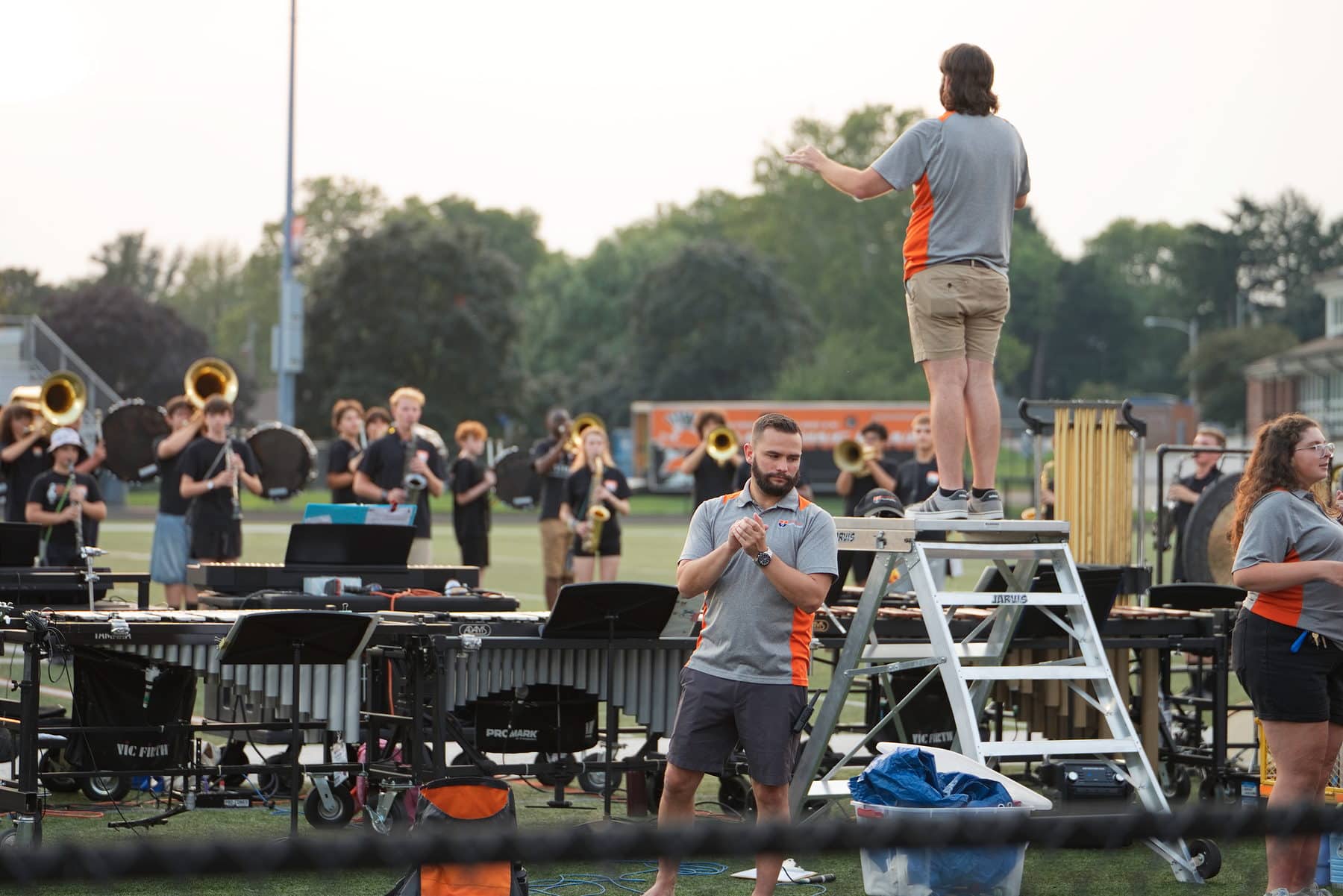 A drum major conducting a marching band from a ladder at rehearsal