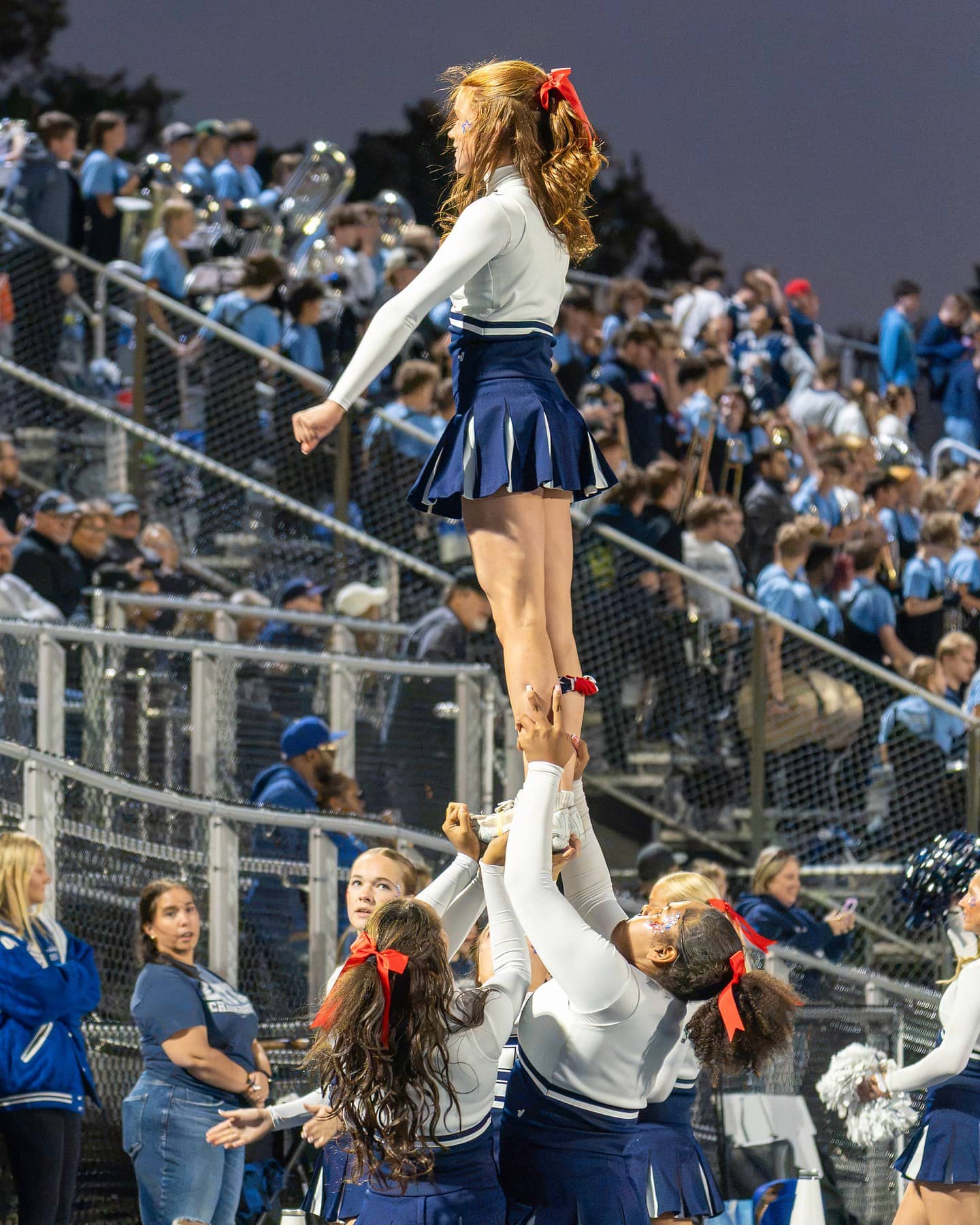 A cheerleading flyer held high beside the packed student stands with the band behind