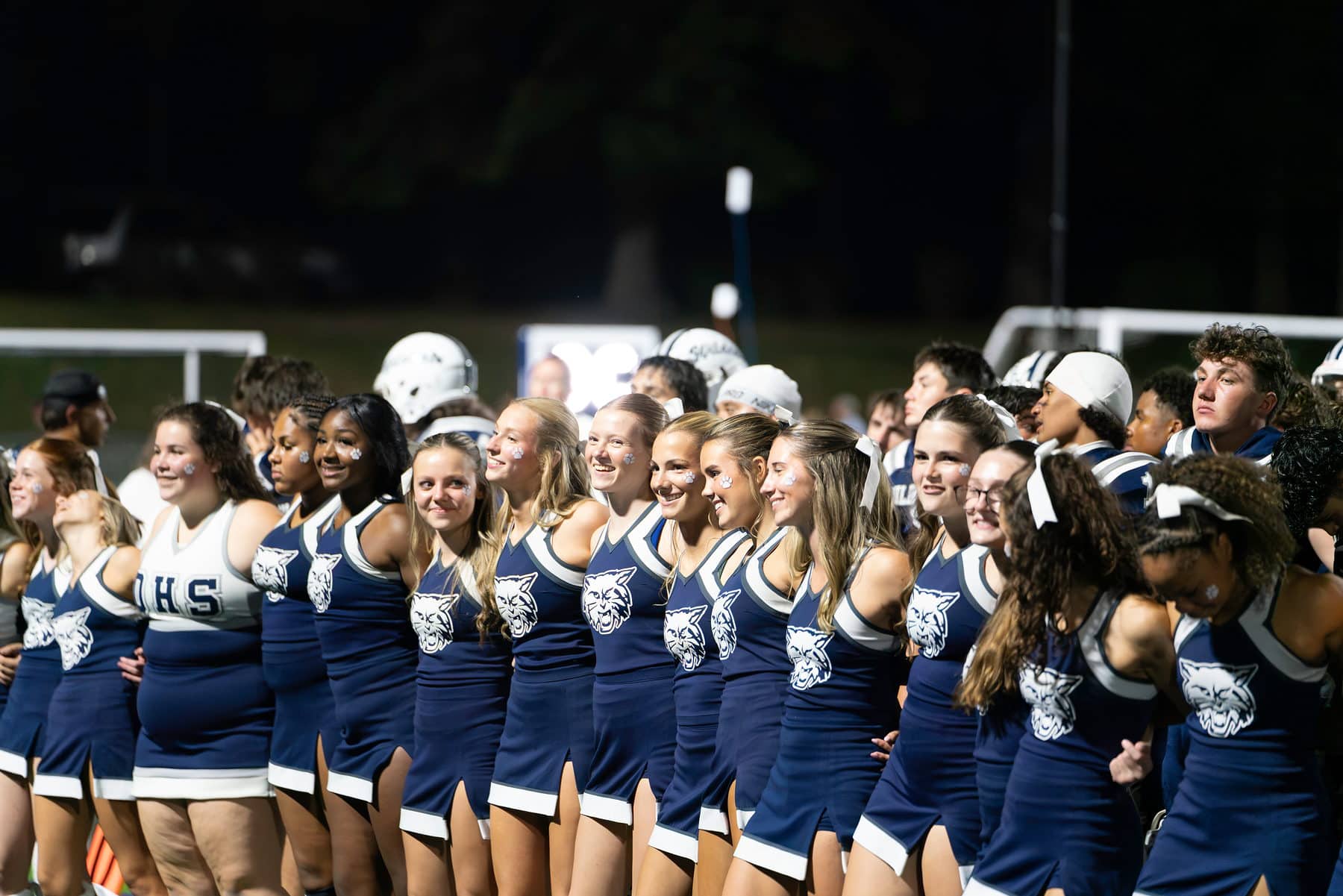 A high school cheer squad on the sideline under the stadium lights
