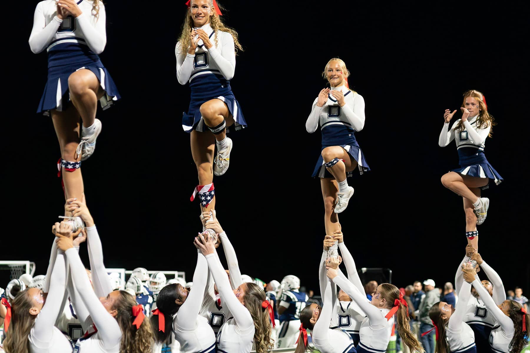 Four cheerleading flyers held up in a stunt line against a black night sky