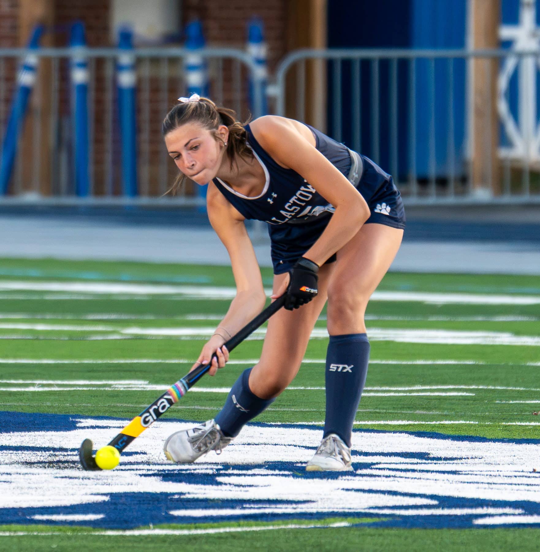 A field hockey player driving the ball forward under stadium lights