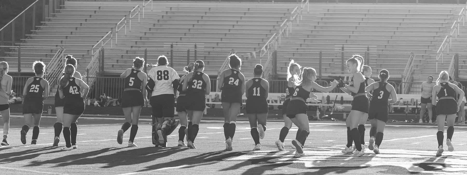 A high school field hockey team standing shoulder to shoulder in a line before a match, in black and white