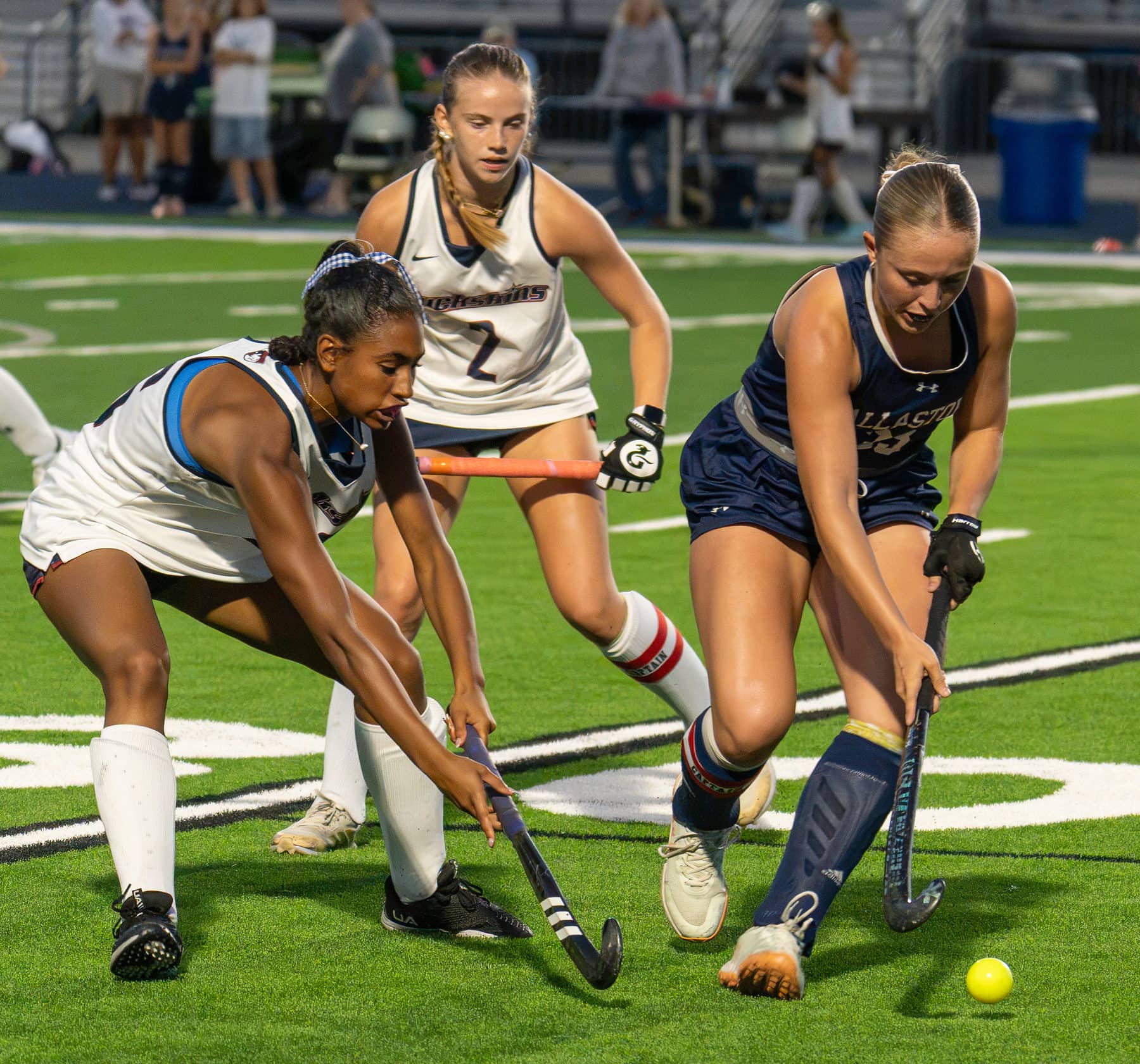 Three field hockey players converging on the same ball at midfield