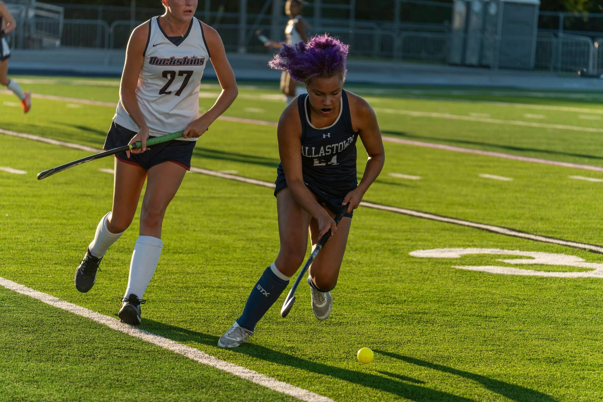 A field hockey player driving the ball in backlit evening sun