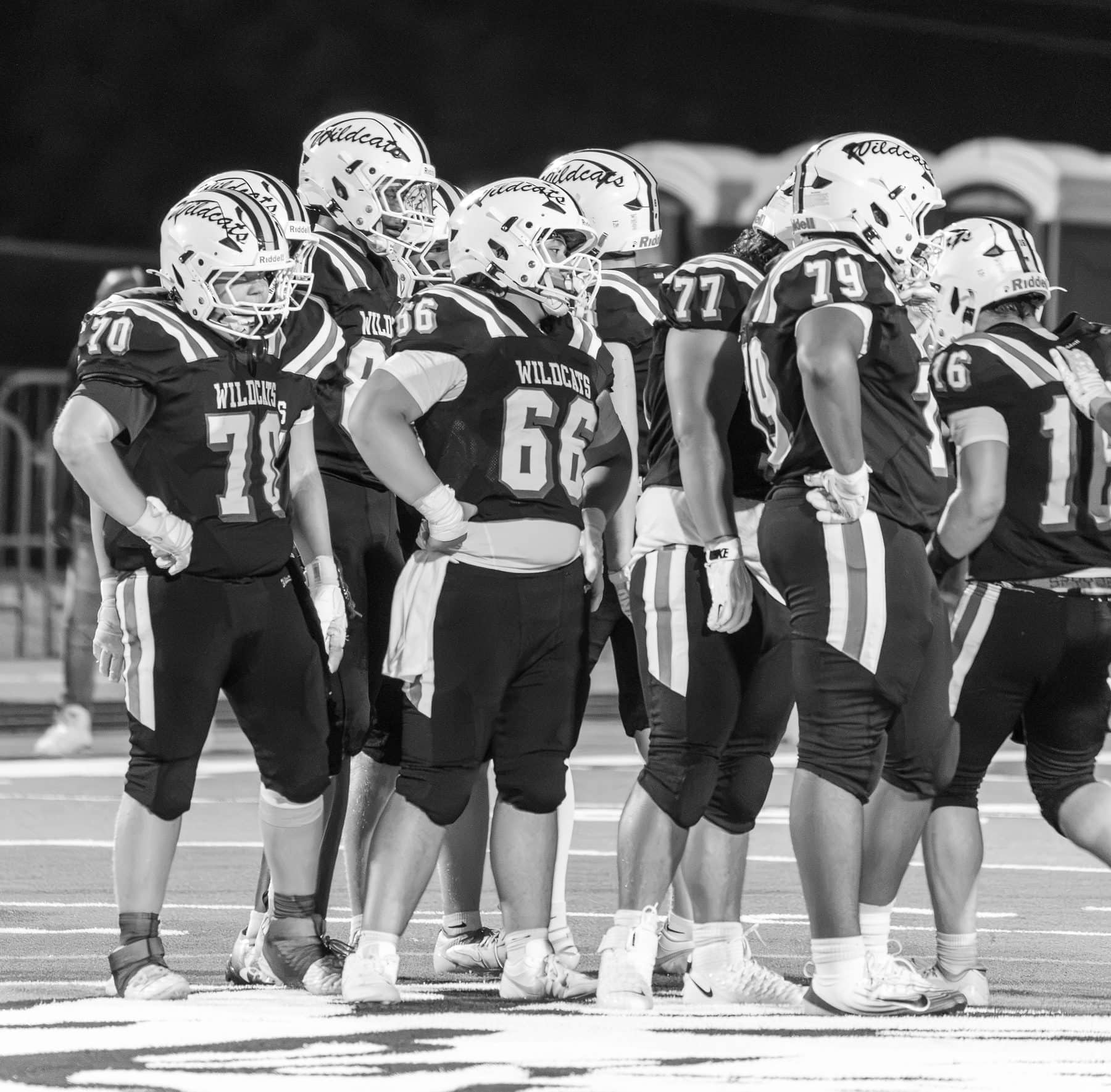 A high school football offense in the huddle, photographed in black and white