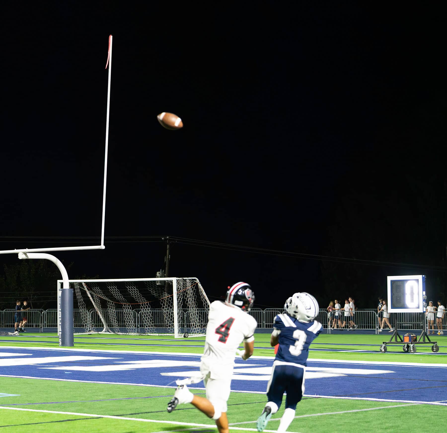 A football in flight against a black night sky above the goalposts