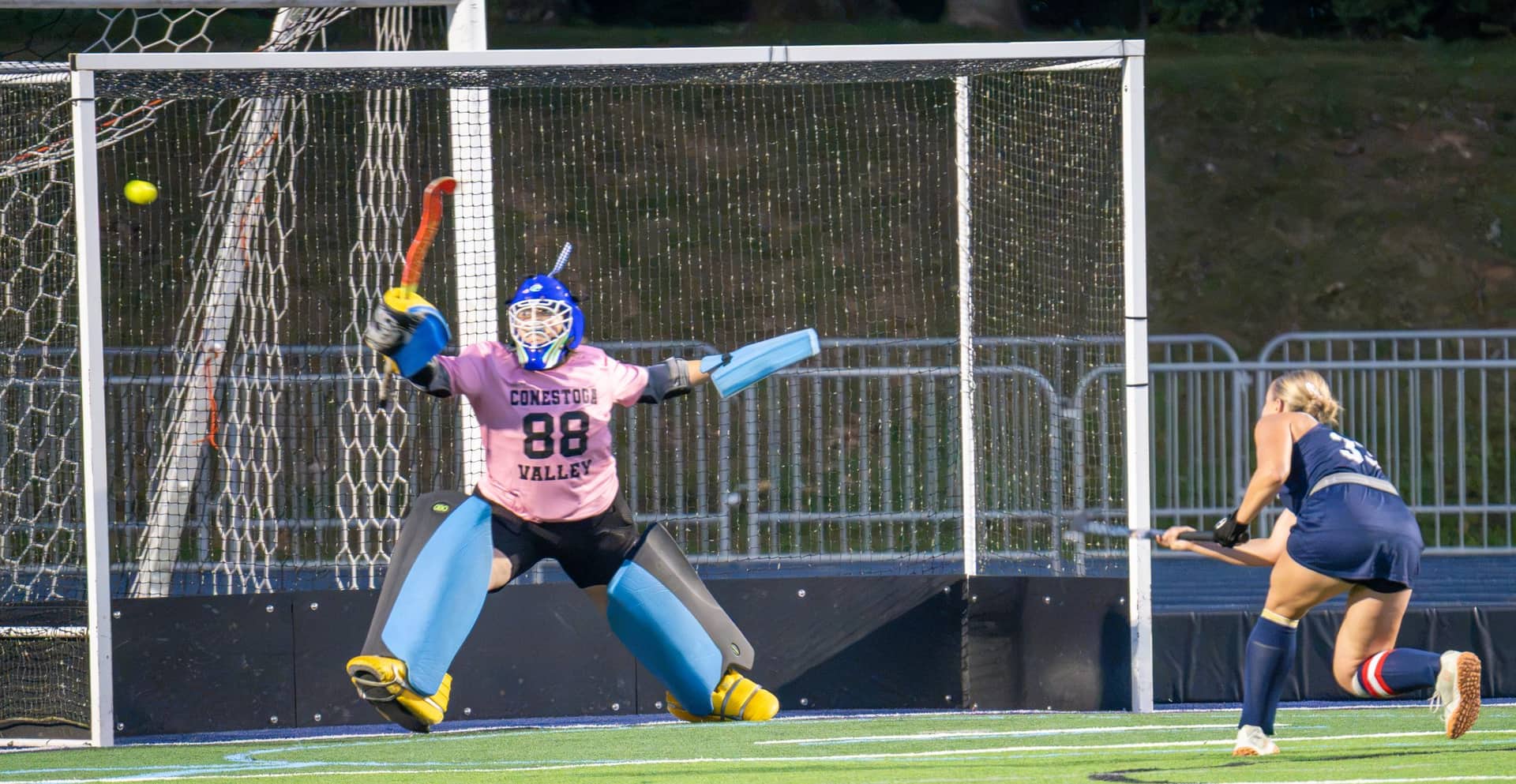 A field hockey goalkeeper making a save under stadium lights
