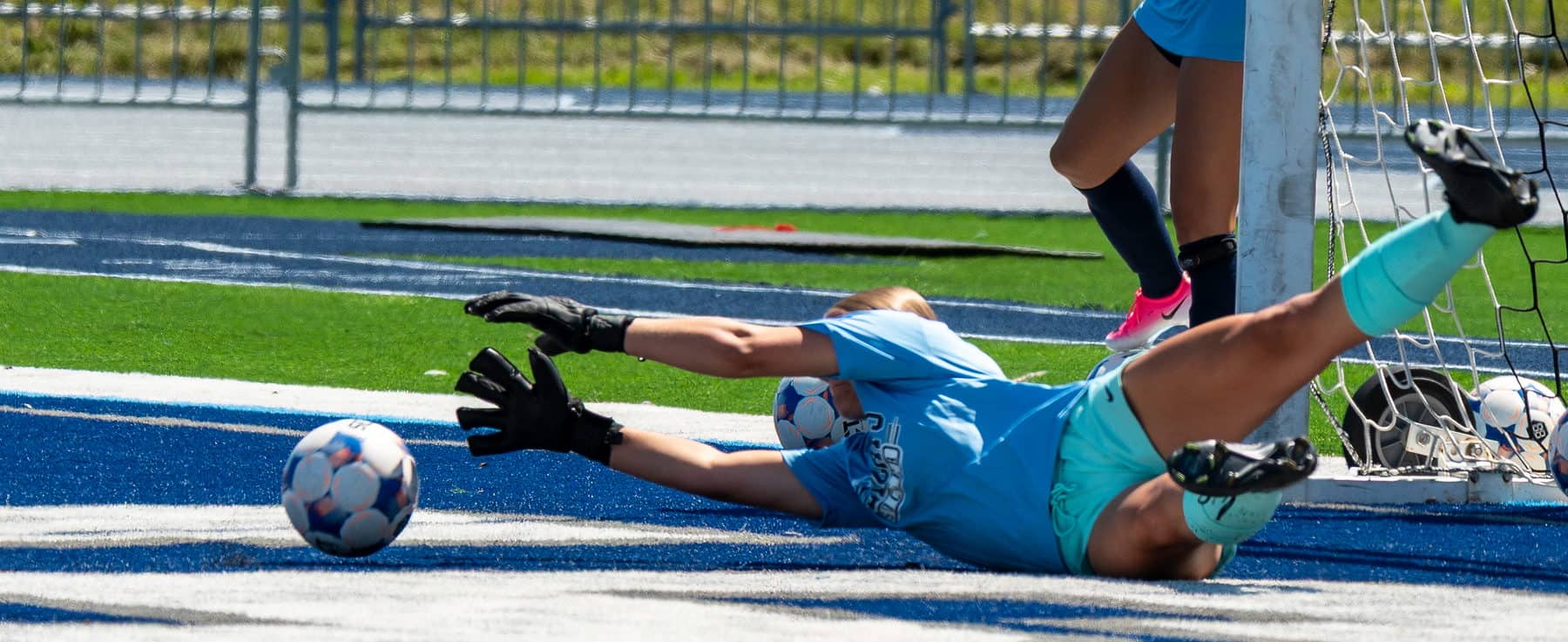 A high school soccer goalkeeper fully extended on the turf after making a save