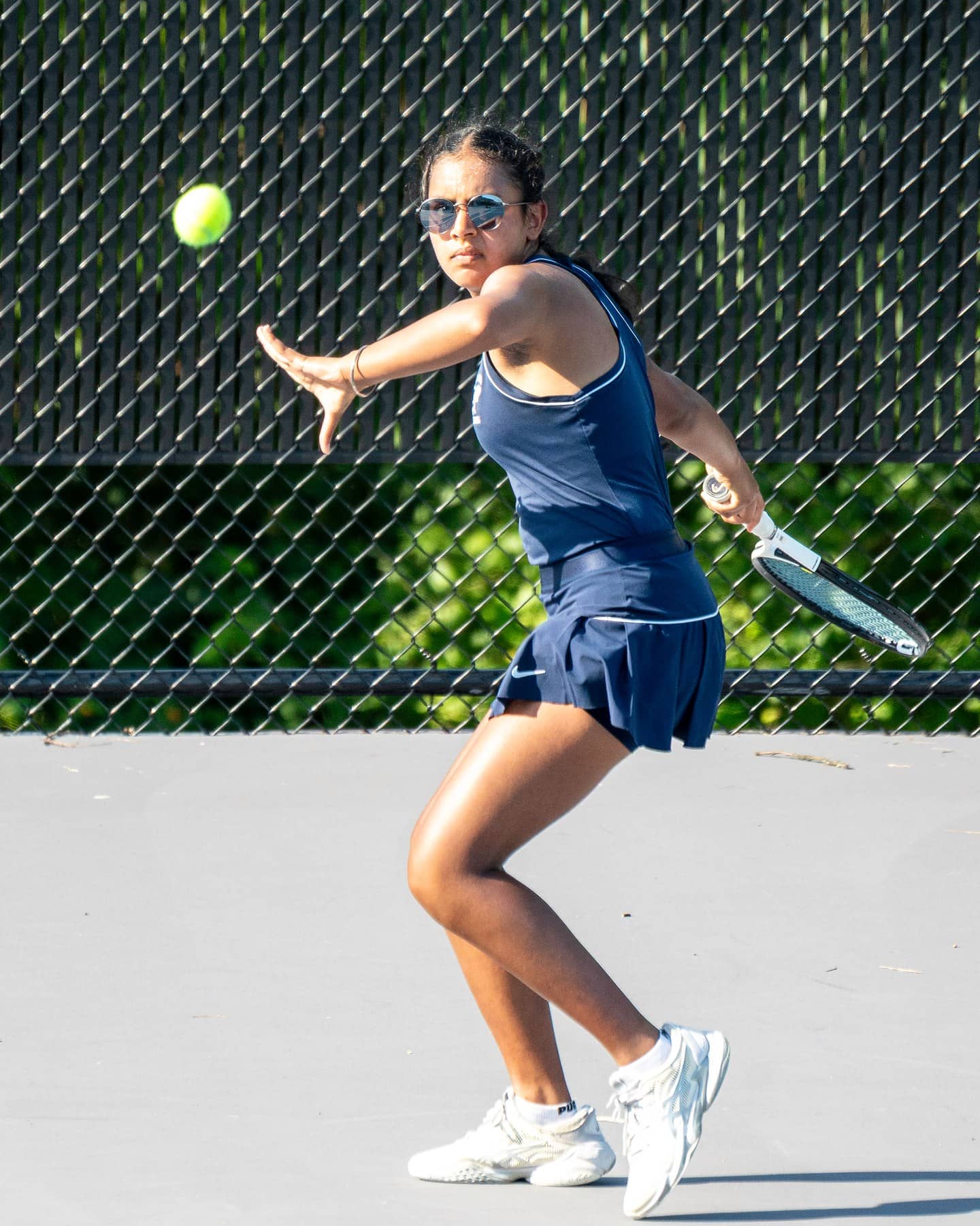 A high school tennis player following through on a forehand with the ball still in the frame