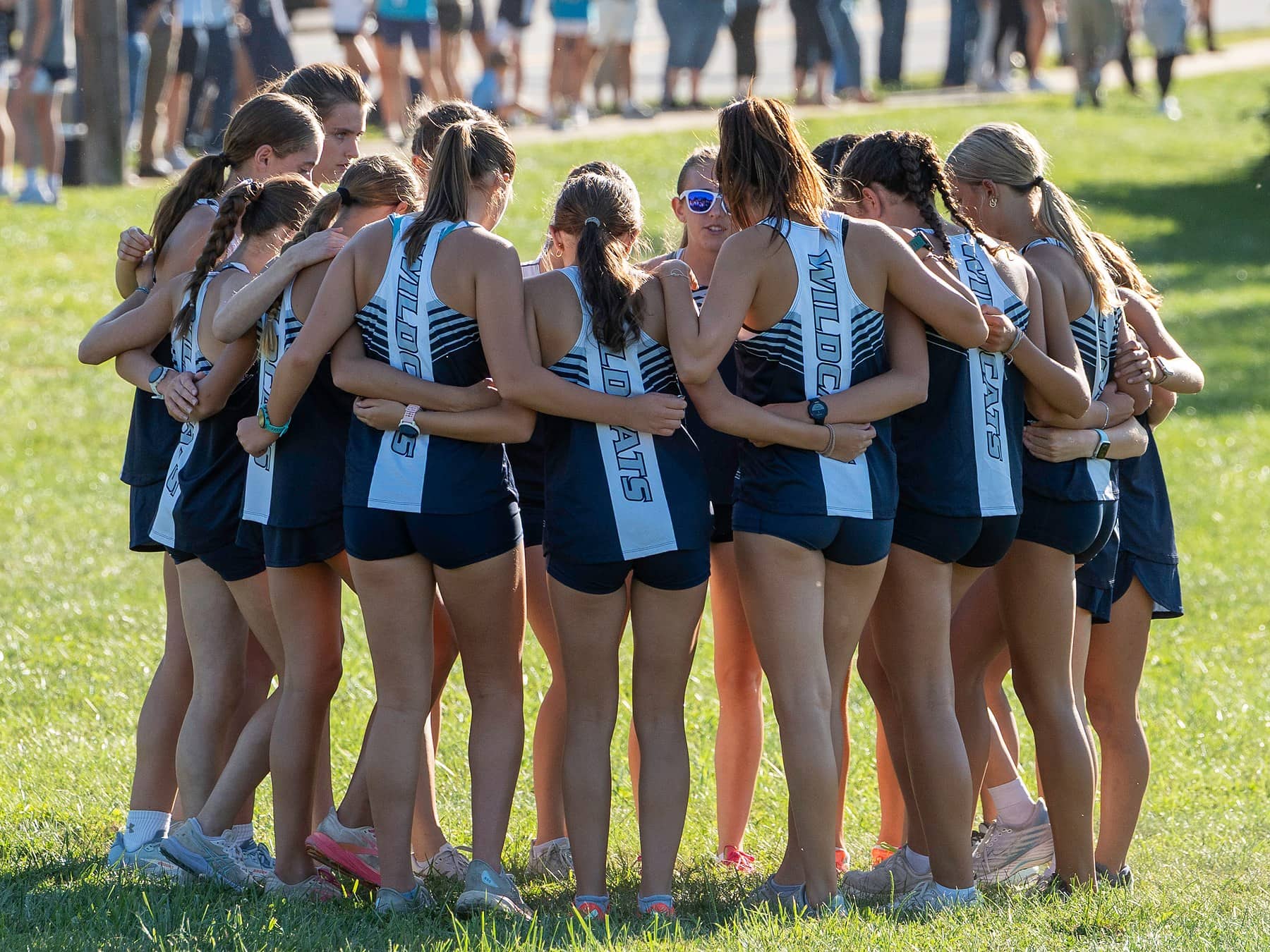 A girls cross country team huddled together with their arms around each other before the race