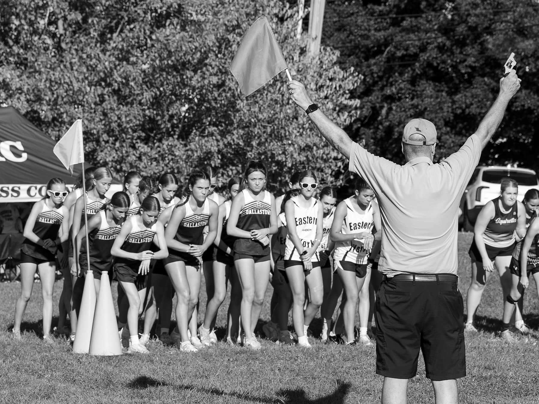 A starter holding up the flag and pistol as a line of cross country runners waits to go, in black and white