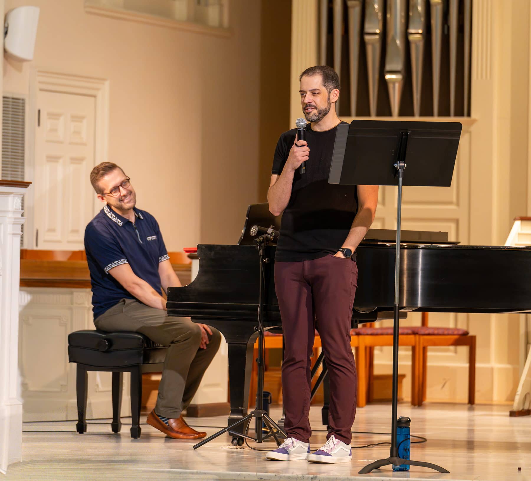 A singer talking to the audience between songs while his accompanist laughs