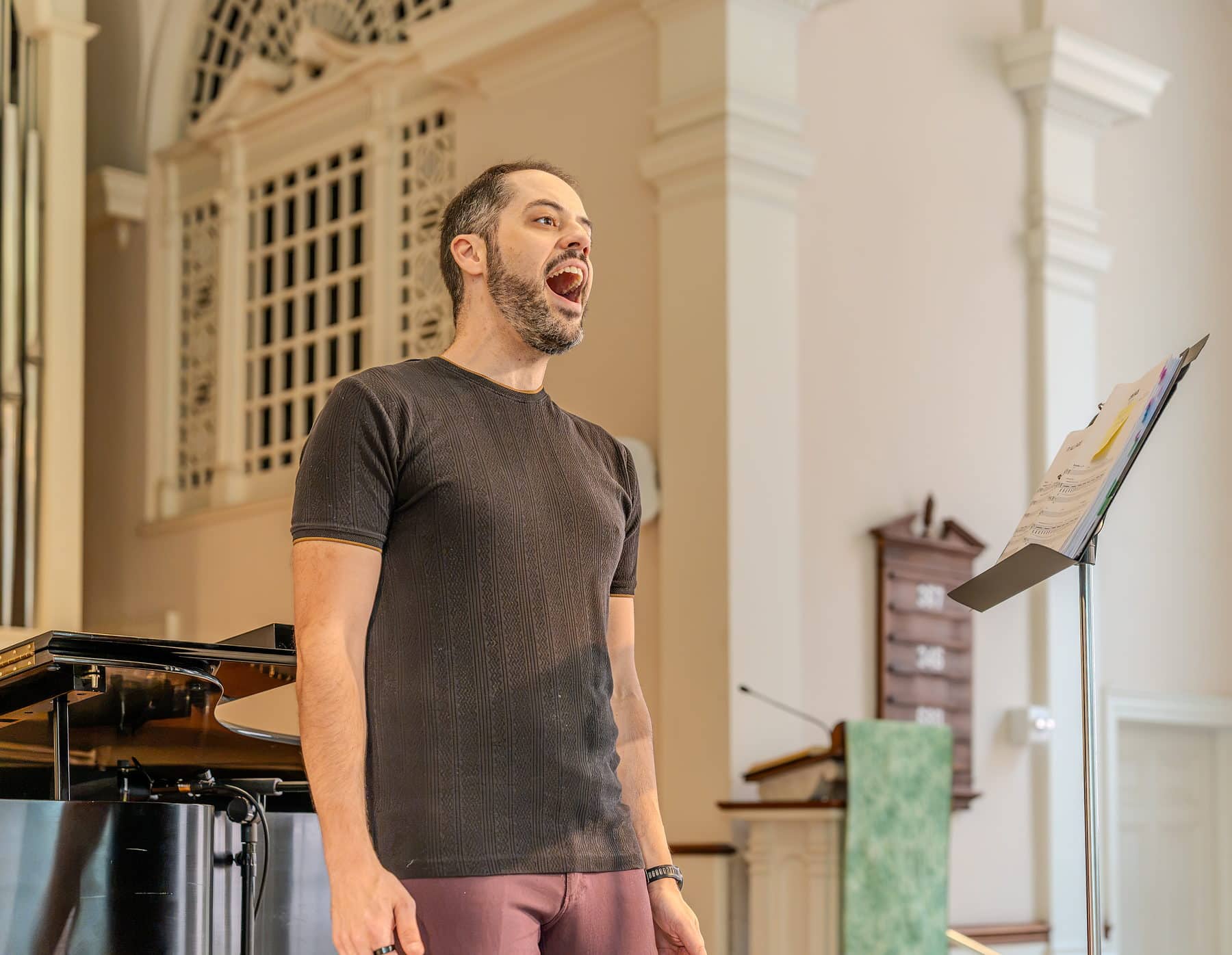 A tenor mid-note during a recital, eyes closed, accompanist behind him