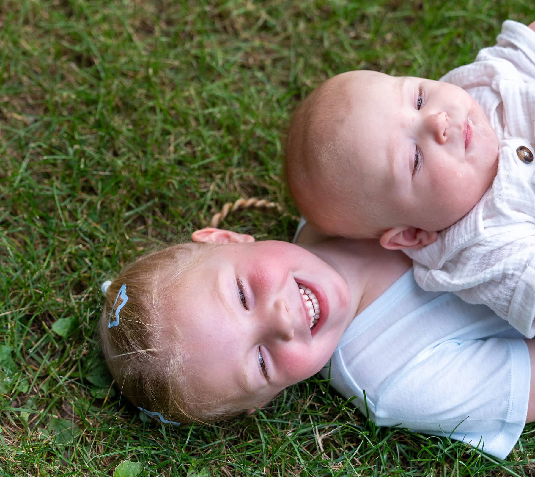 A brother and sister lying sideways in the grass, both laughing