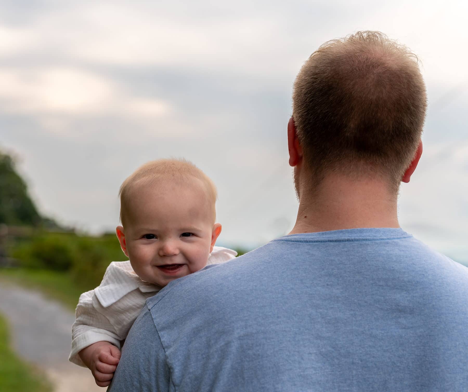 A baby looking back over his father's shoulder into the camera