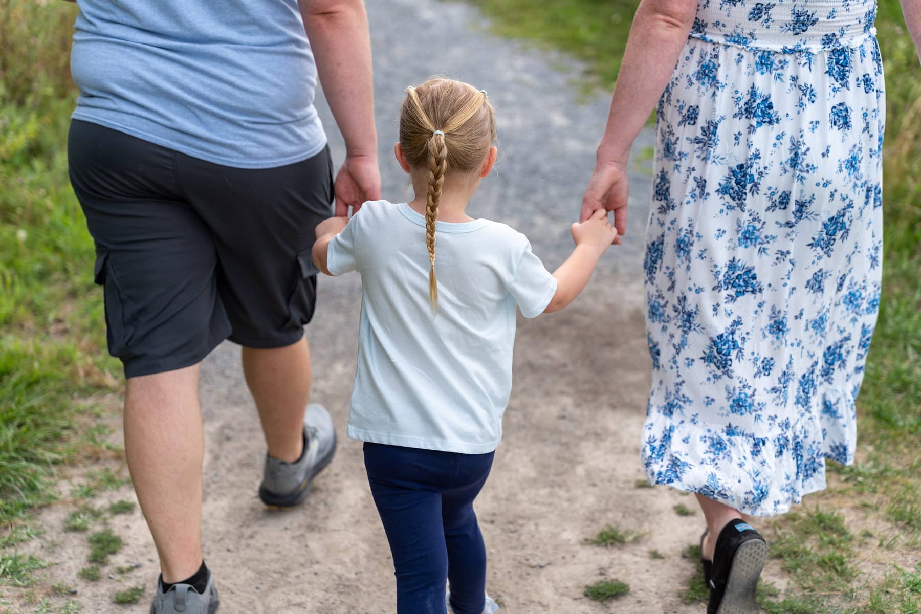 A family of three walking away hand in hand down a wooded trail in York County