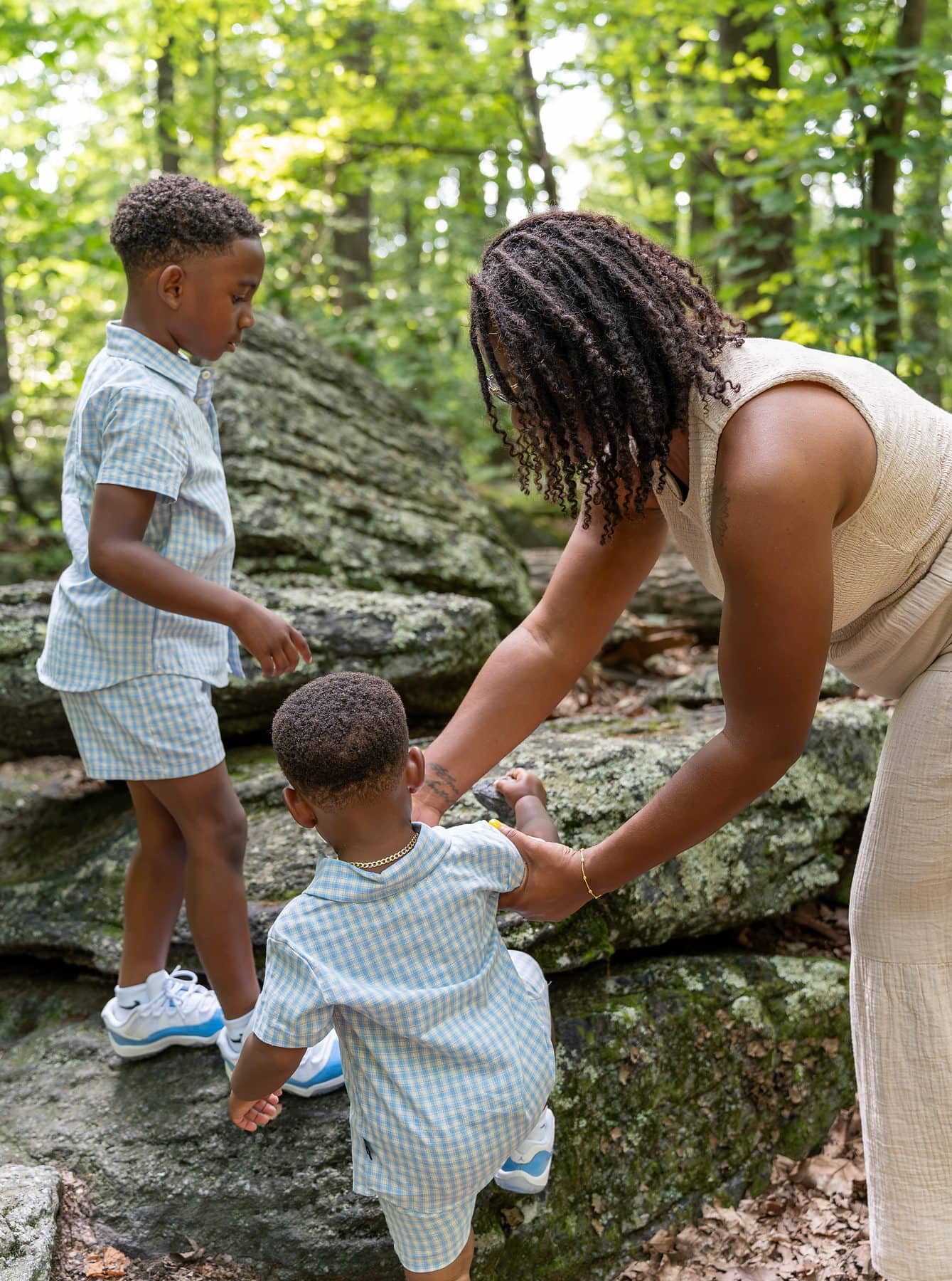 A mother helping her two sons scramble up a rock outcrop on a trail