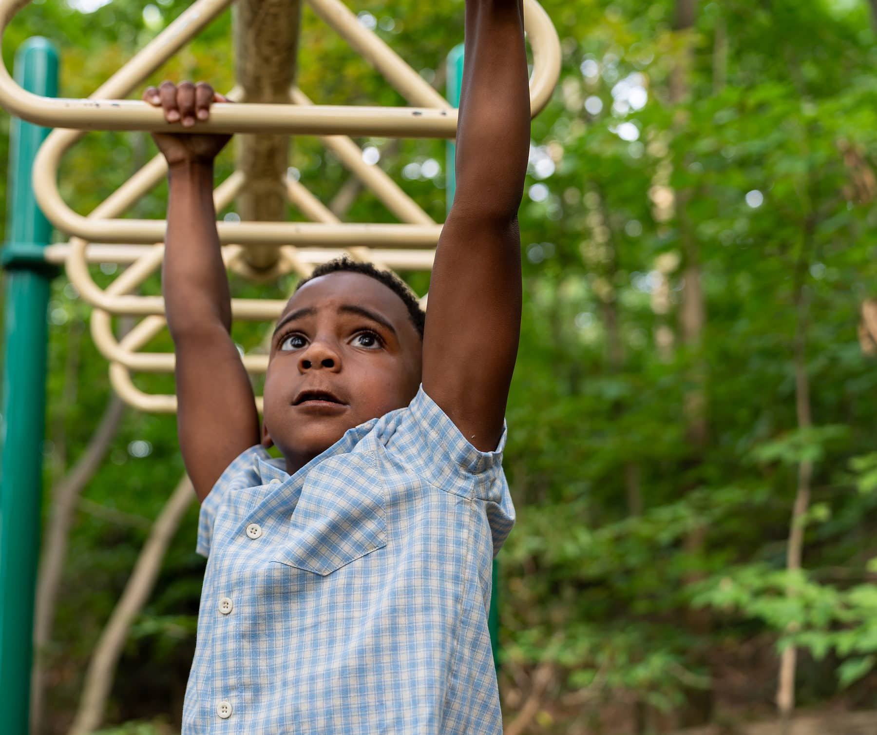 A boy hanging from playground bars and looking up at his own hands