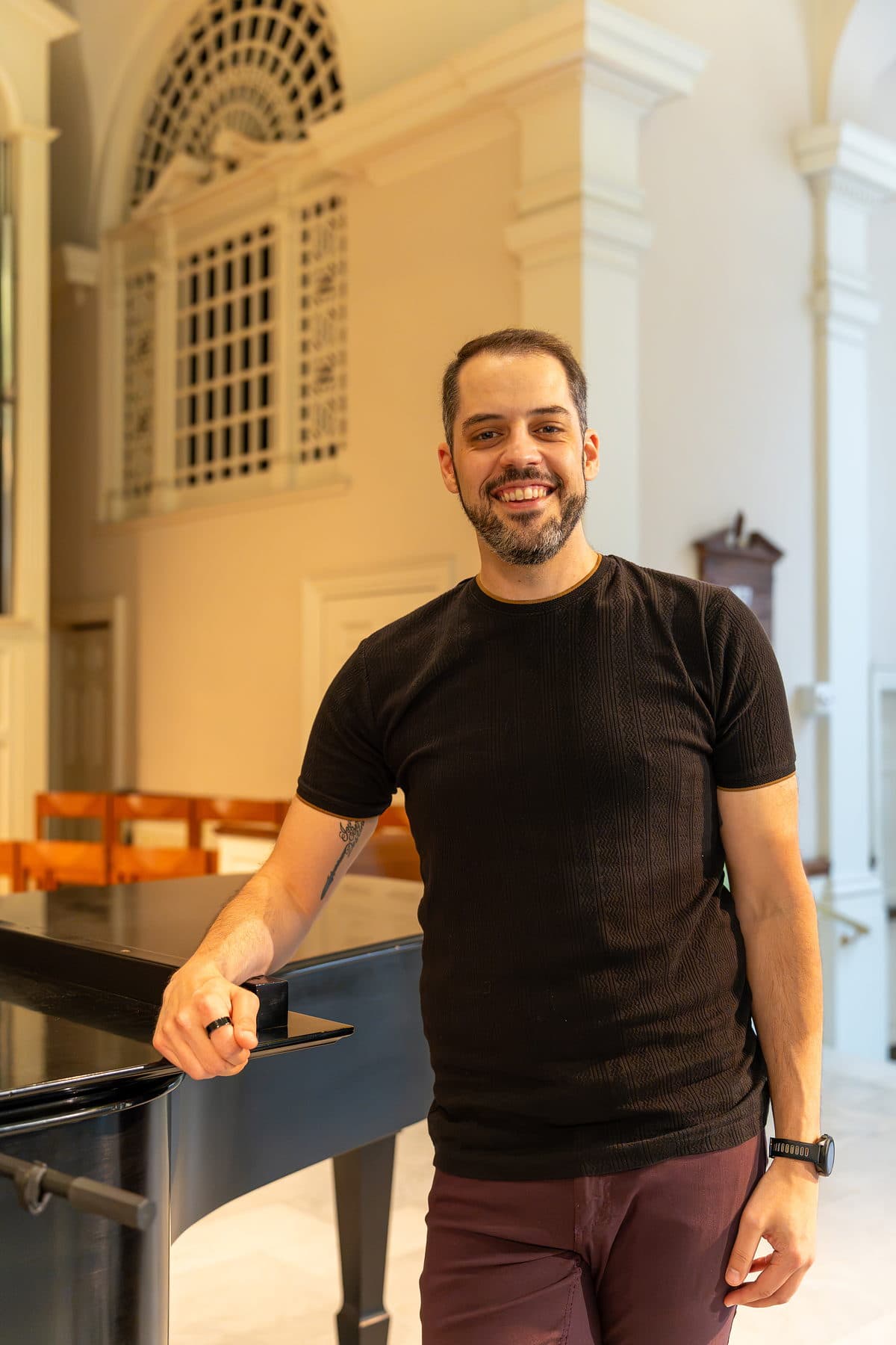 A relaxed editorial portrait of a performer in window light beside a grand piano